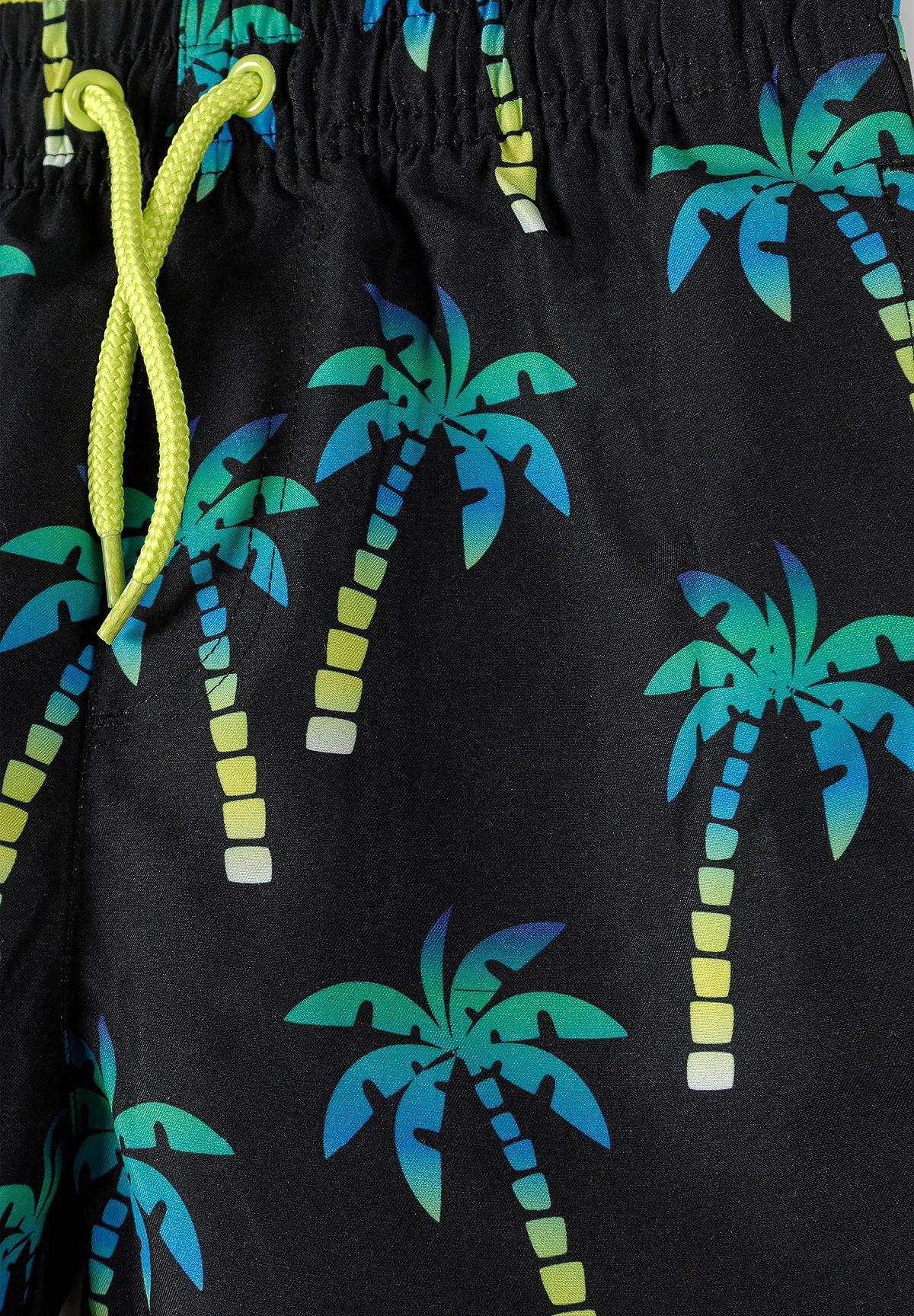 Close-up of black swim shorts showing a lime drawcord and blue-to-teal palms with lime striped trunks.