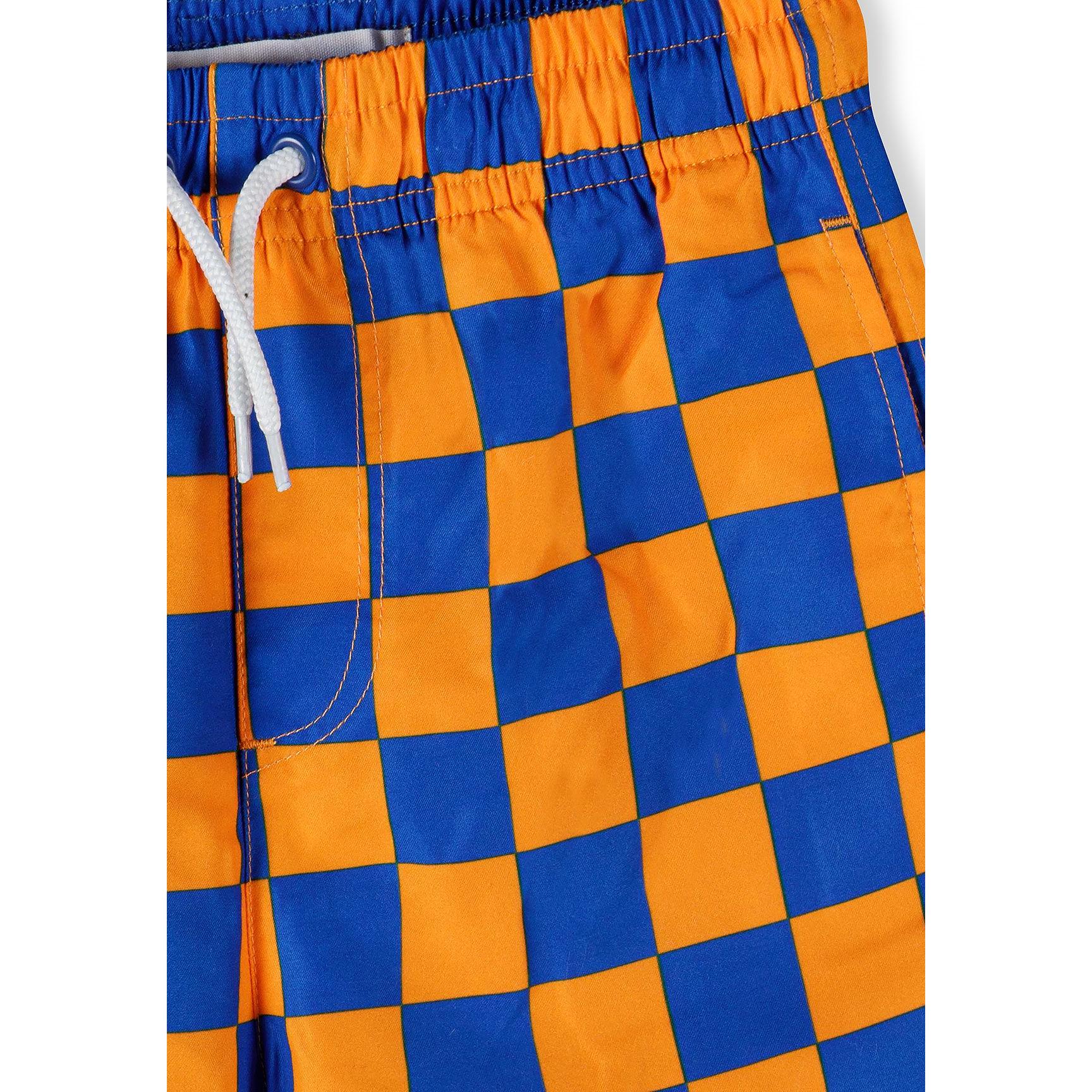 Close-up detail of orange and blue checkerboard pattern swim shorts showing elastic waistband with white drawstring cord