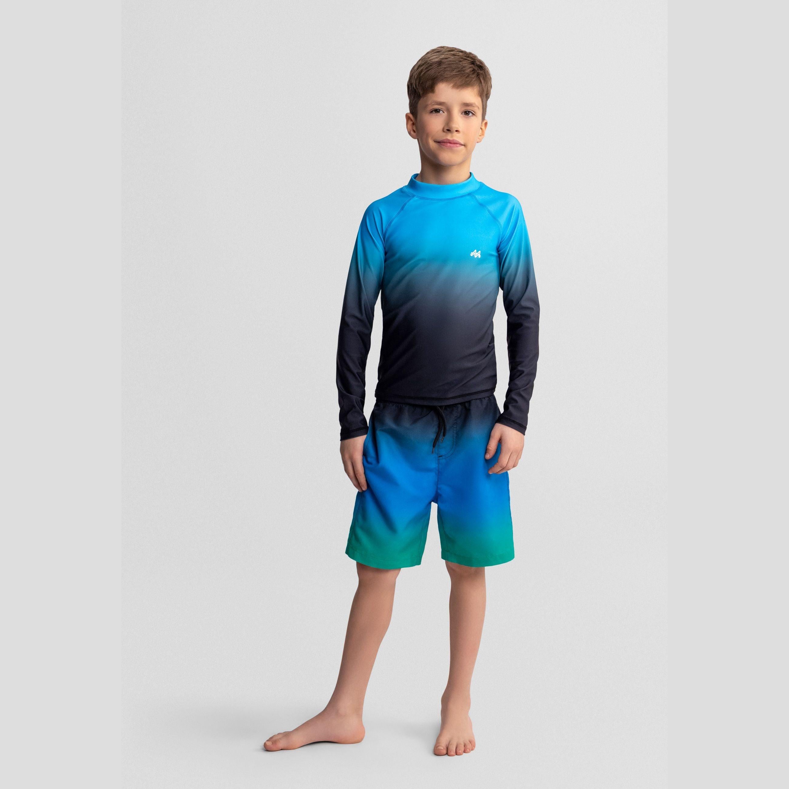 Boy wearing blue ombré long sleeve rash guard and matching swim shorts, standing against white background