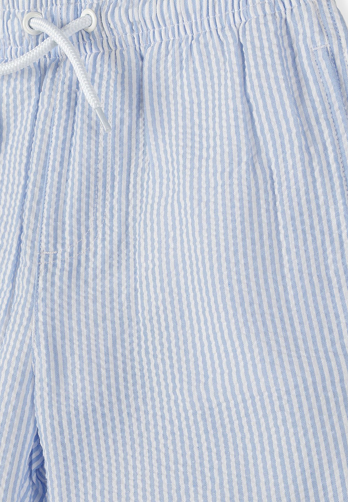 Close-up of blue and white striped swim shorts showing rippled fabric and white drawstring eyelets.