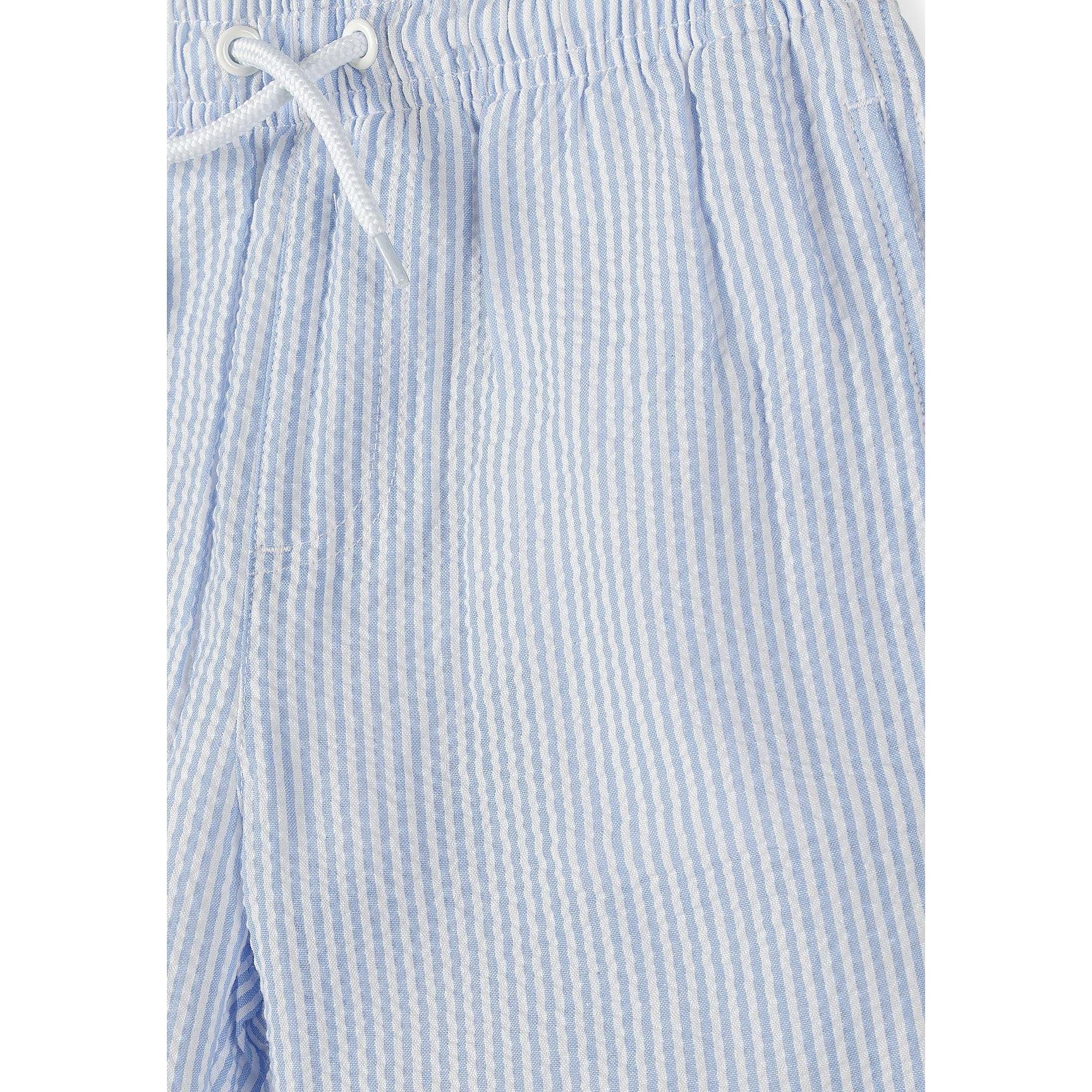 Close-up detail of light blue striped swim shorts showing elasticated waistband with white drawstring and vertical stripe pattern texture