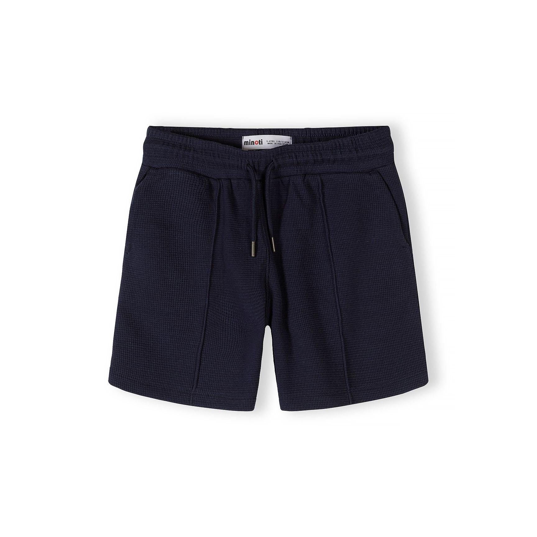 Close-up detail of navy polo shirt collar and button placket showing Minoti label and textured cotton fabric