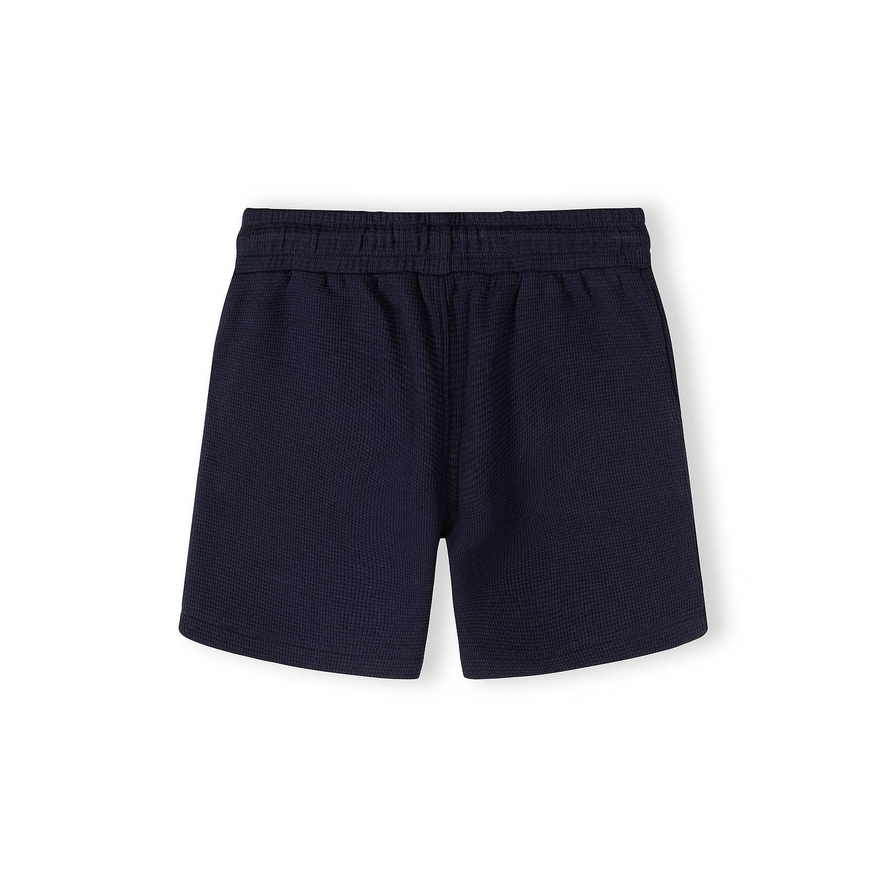 Close-up detail of navy polo shirt collar and button placket showing Minoti label and textured cotton fabric