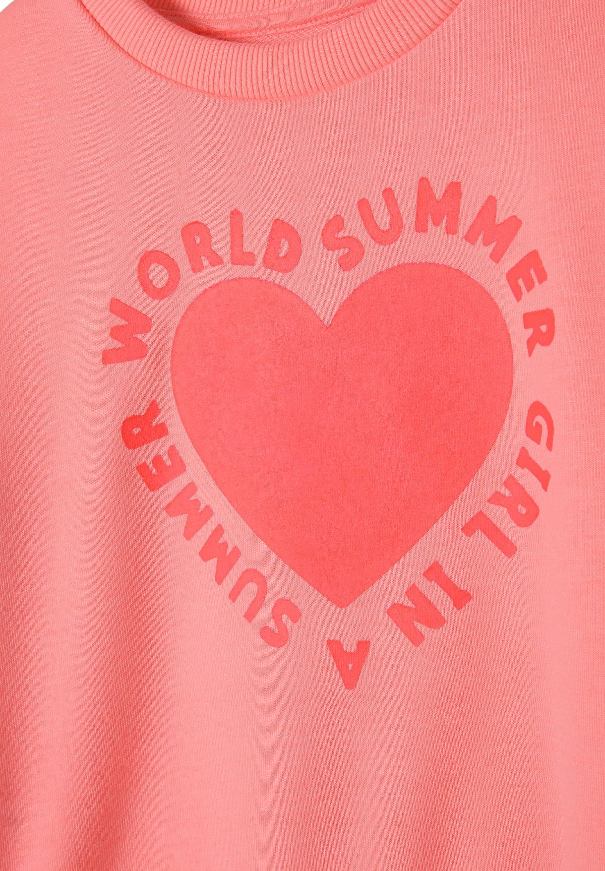 Close-up of coral heart with circular WORLD SUMMER GIRL IN A SUMMER text on sweatshirt.