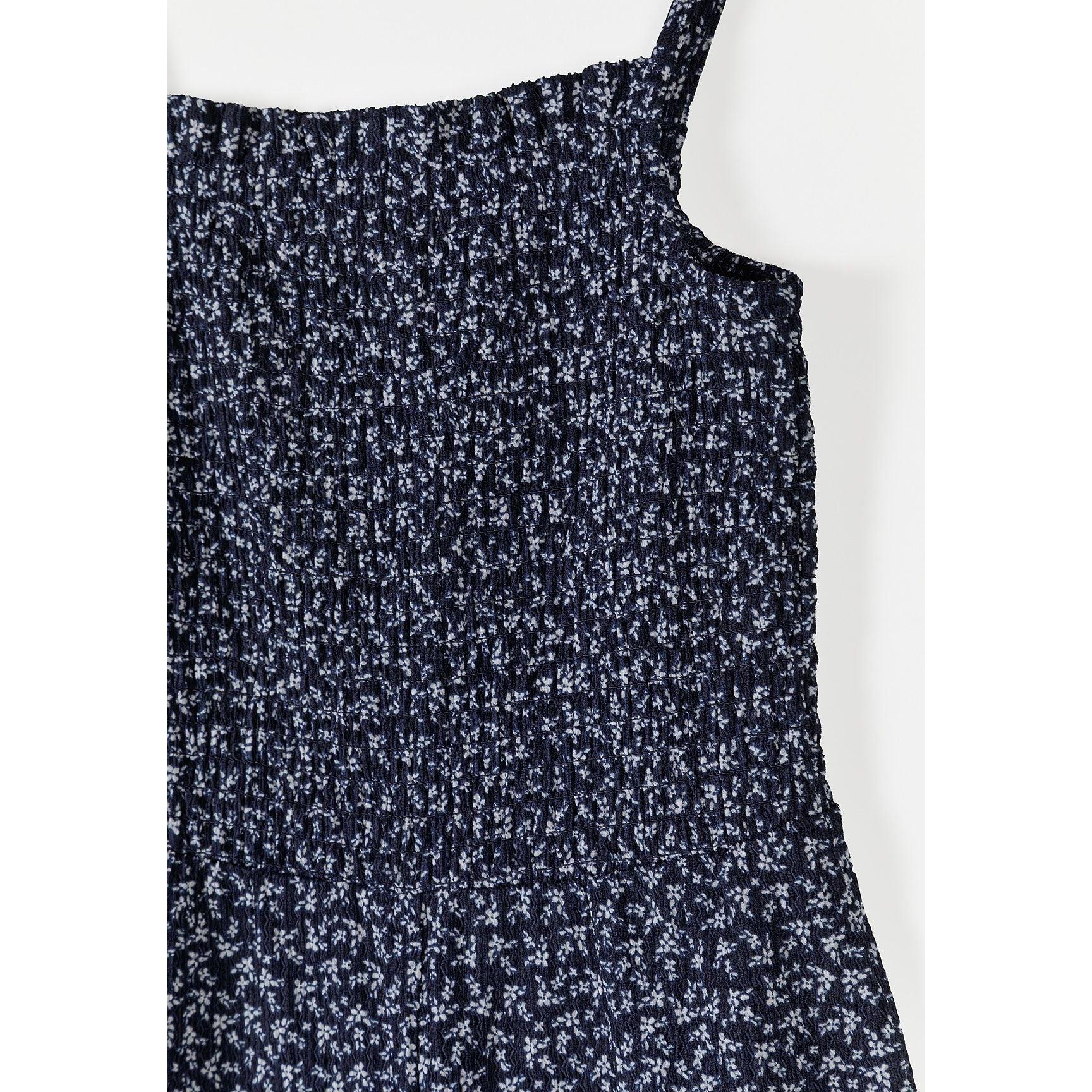 Close-up detail shot of navy jumpsuit fabric showing small white floral print pattern and smocked bodice texture on white background