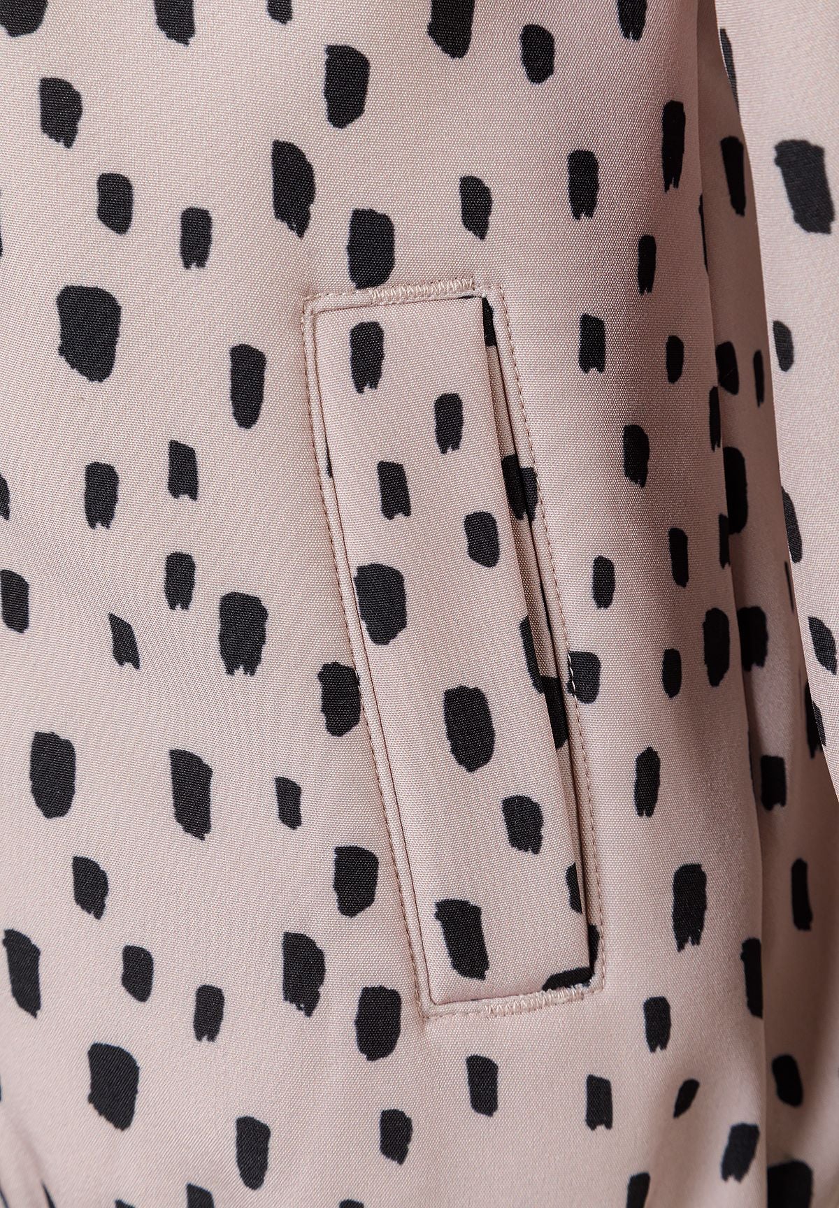 Detail of a girls' softshell jacket in pink with black spots, featuring a front pocket.