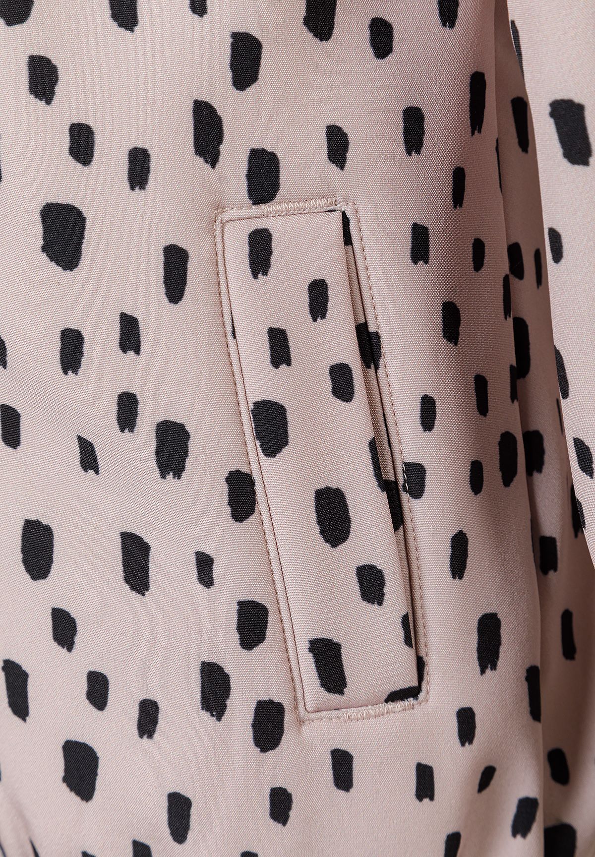 Close-up of vertical side pocket in pale pink jacket with black dash print.