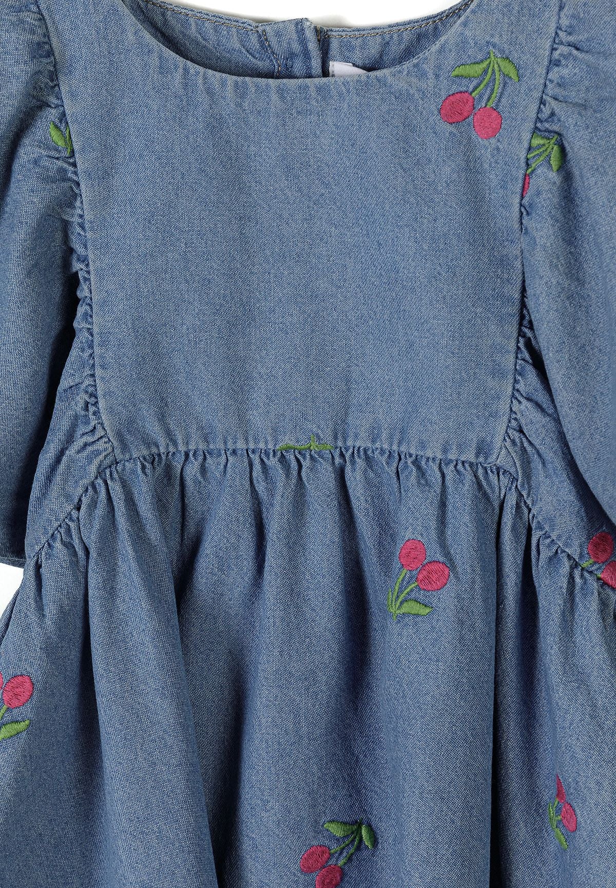 Detail of girls' denim dress in blue with cherry embroidery and gathered skirt.