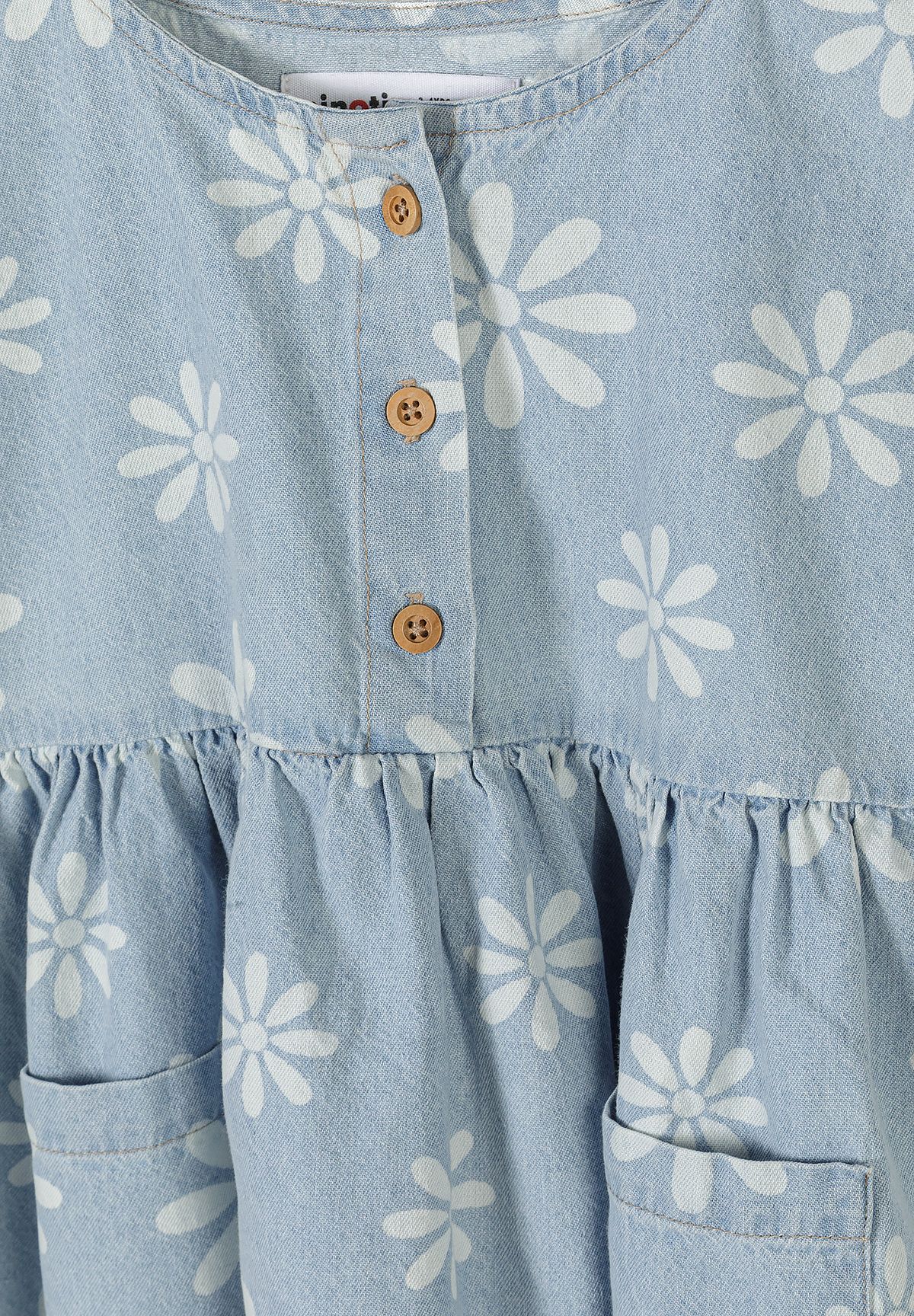 Detail of girls' chambray dress with floral print, button fastening, and ruffled skirt.
