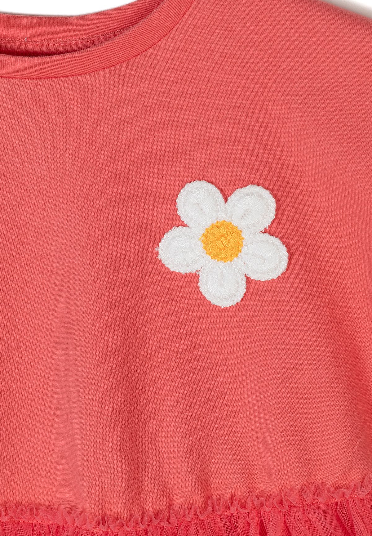 Close-up of coral dress bodice showing a single white five-petal daisy with yellow textured centre.