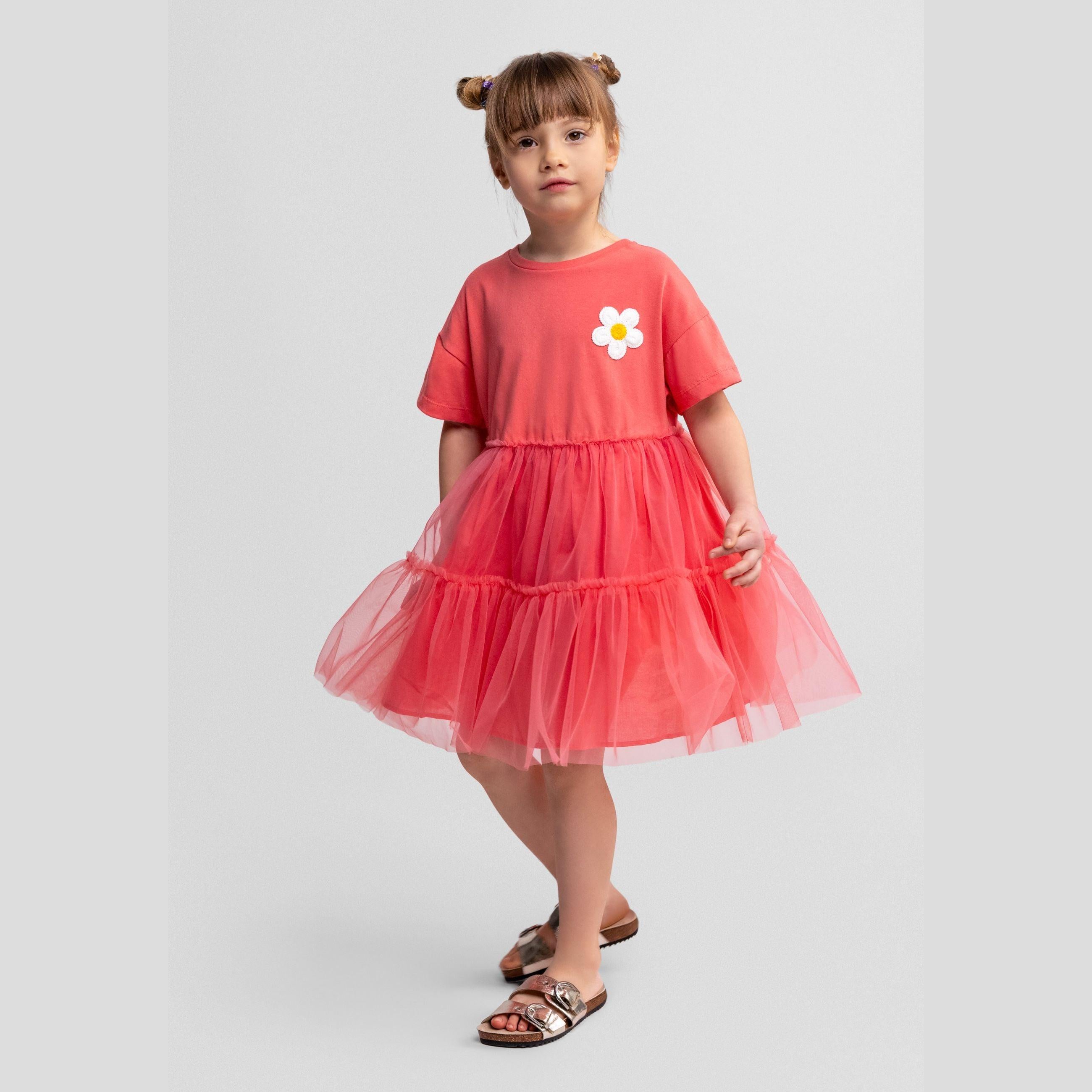Young girl wearing coral tulle dress with white daisy embroidery, standing against white background, full body view showing layered tulle skirt