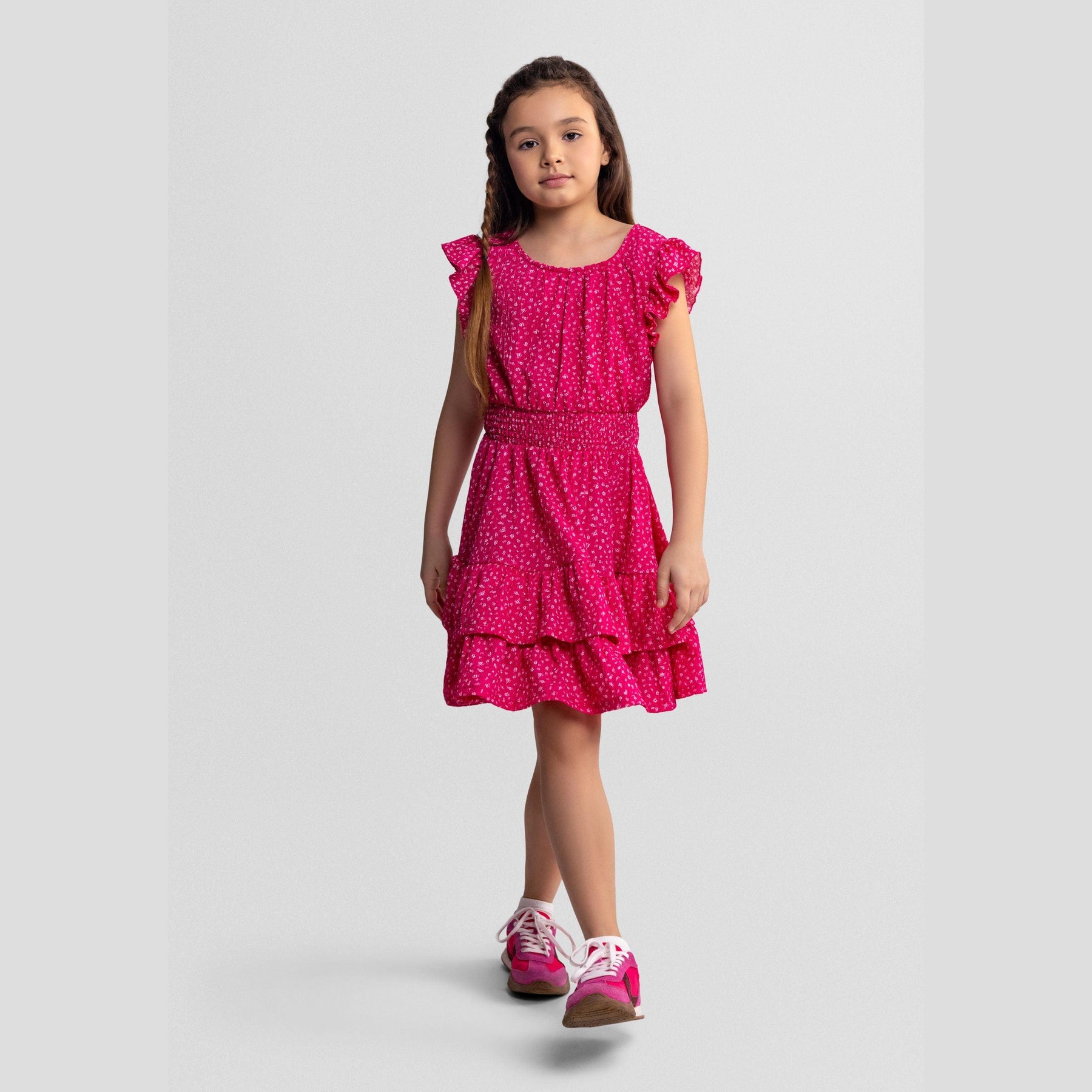 Pink floral dress laid flat showing frill sleeves, elasticated waist, tiered skirt design and white floral print pattern on pink fabric