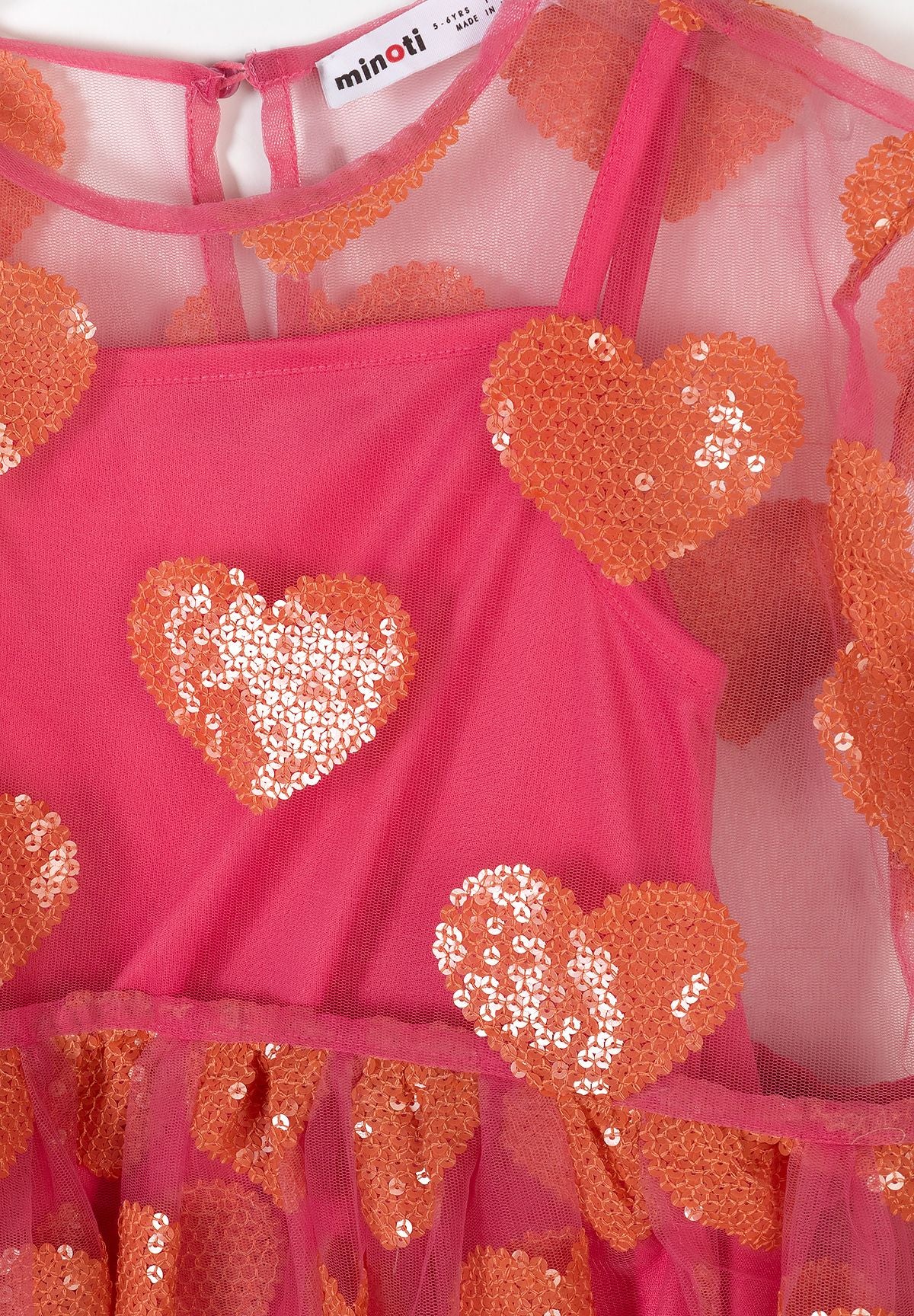 Close-up detail of Minoti dress label and pink tulle fabric with orange sequin heart embellishments showing texture and sparkle