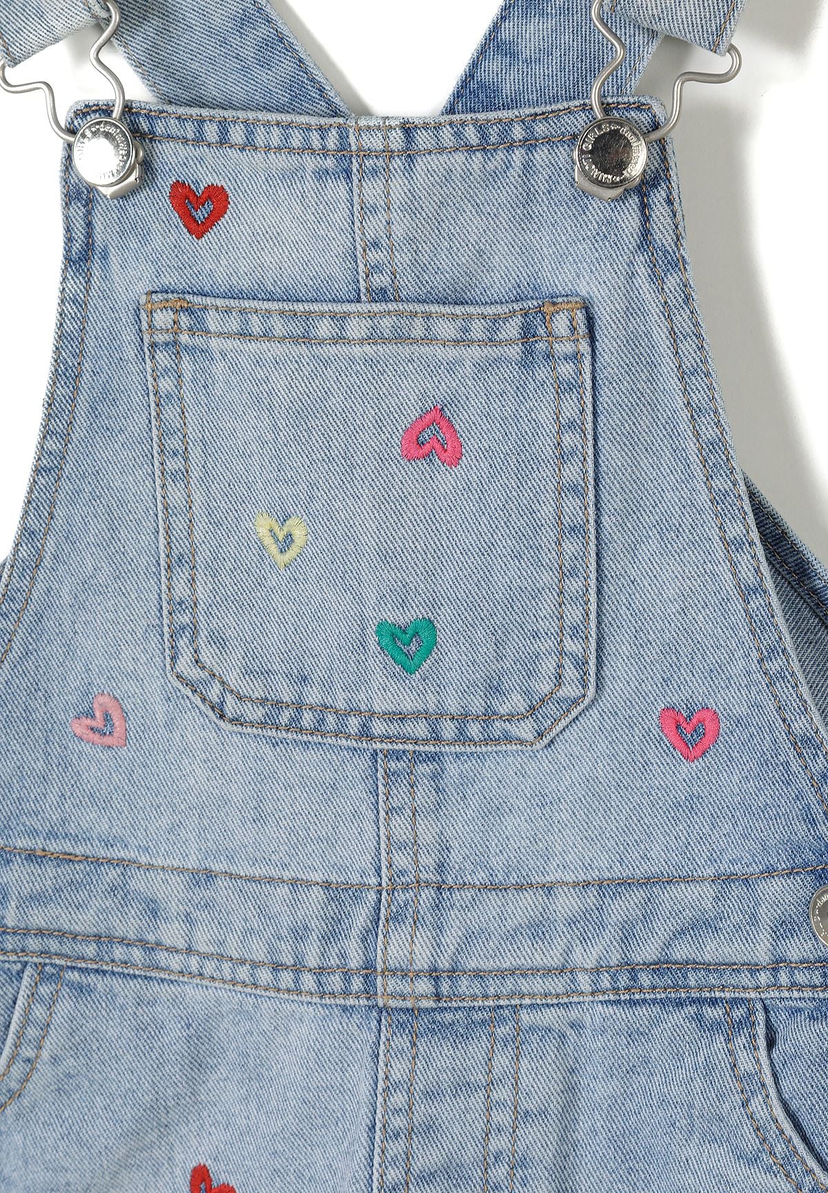 Detail of girls' blue denim dungaree with colorful heart embroidery.