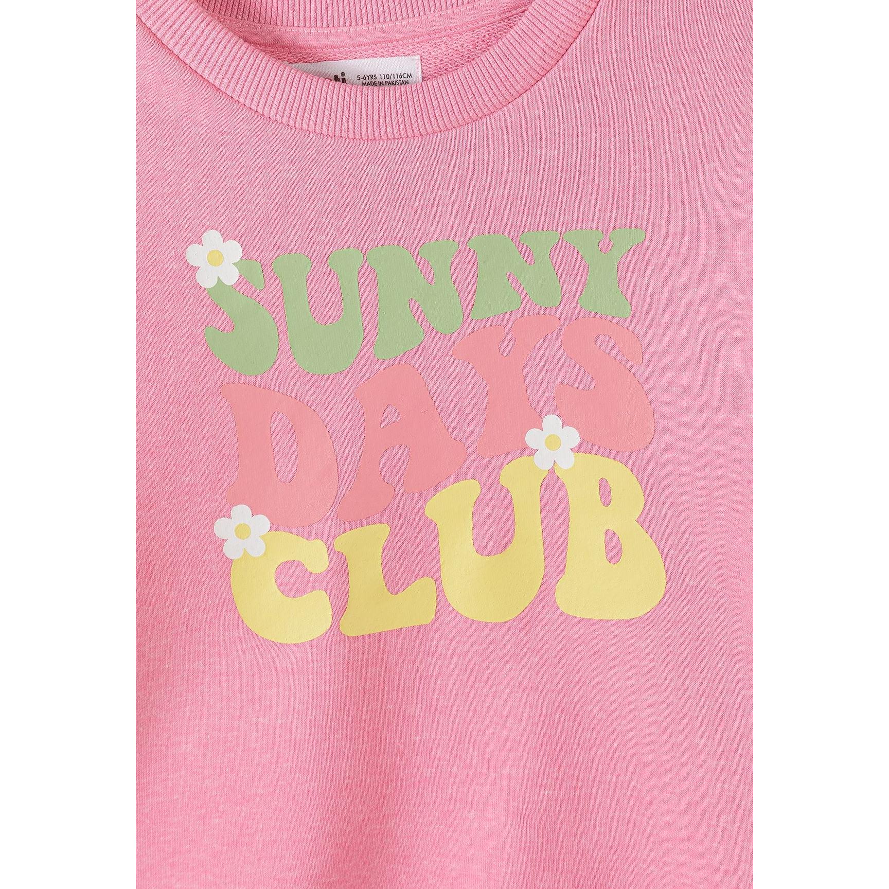 Close-up detail of coral pink sweatshirt showing Hello Flower text with smiling daisy graphics and Minoti label at neckline