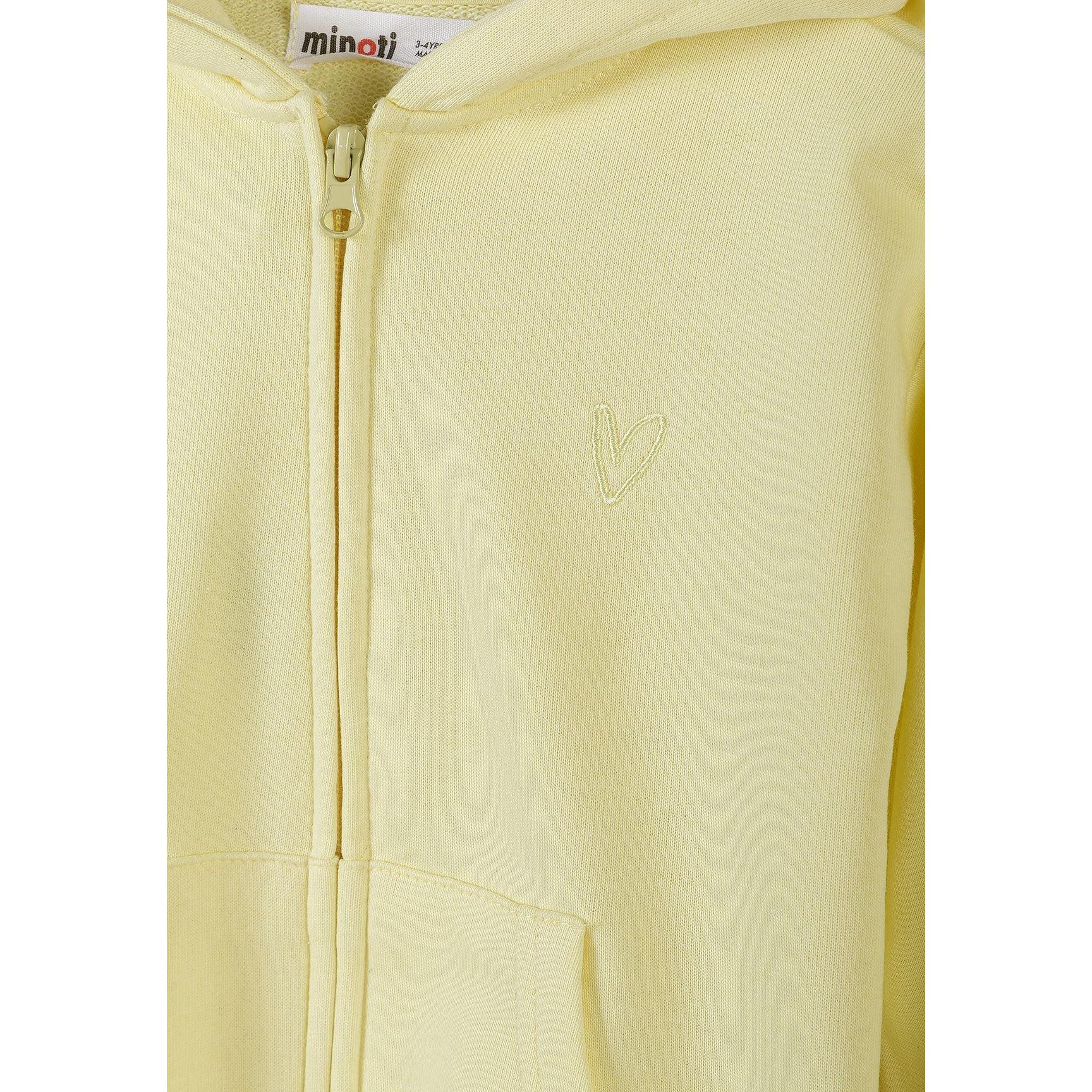Detail shot showing Minoti label and embroidered heart design on pale yellow hoodie fabric with zip fastening visible