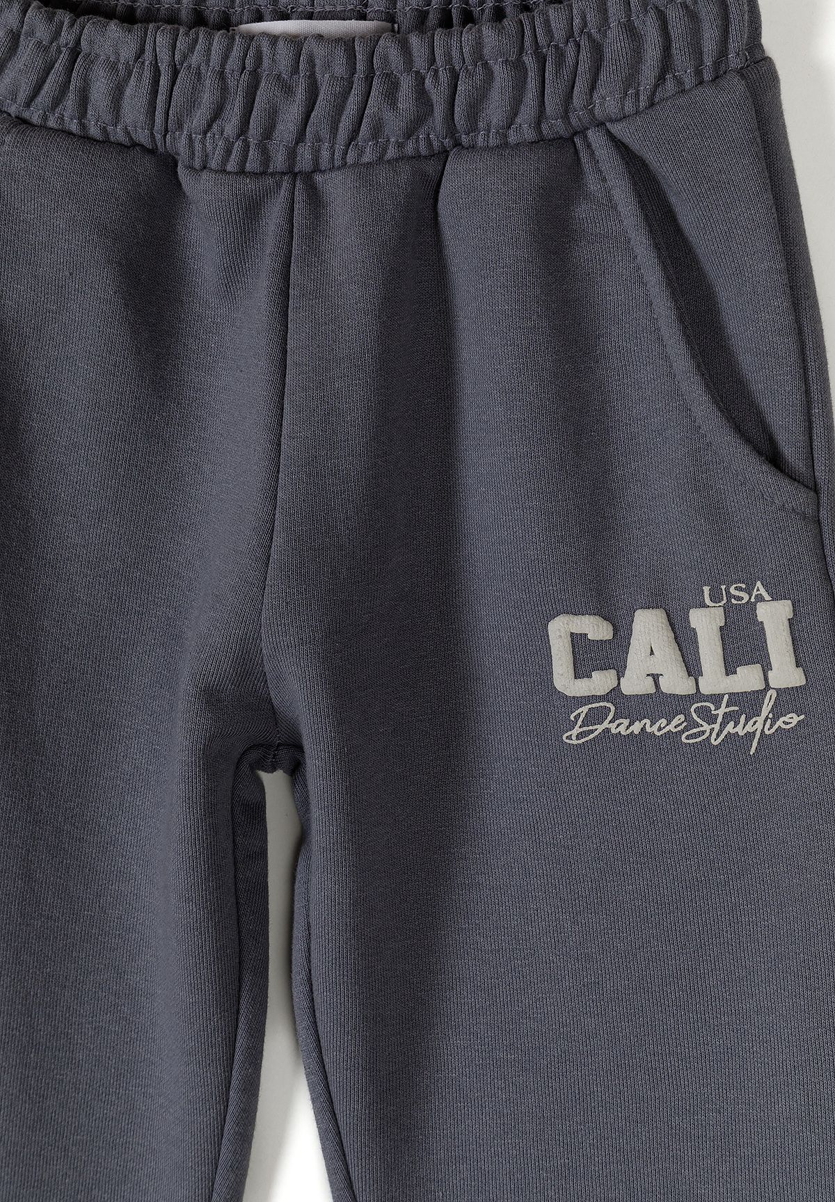 Close-up of blue-grey joggers' pocket, gathered waist and Cali print.