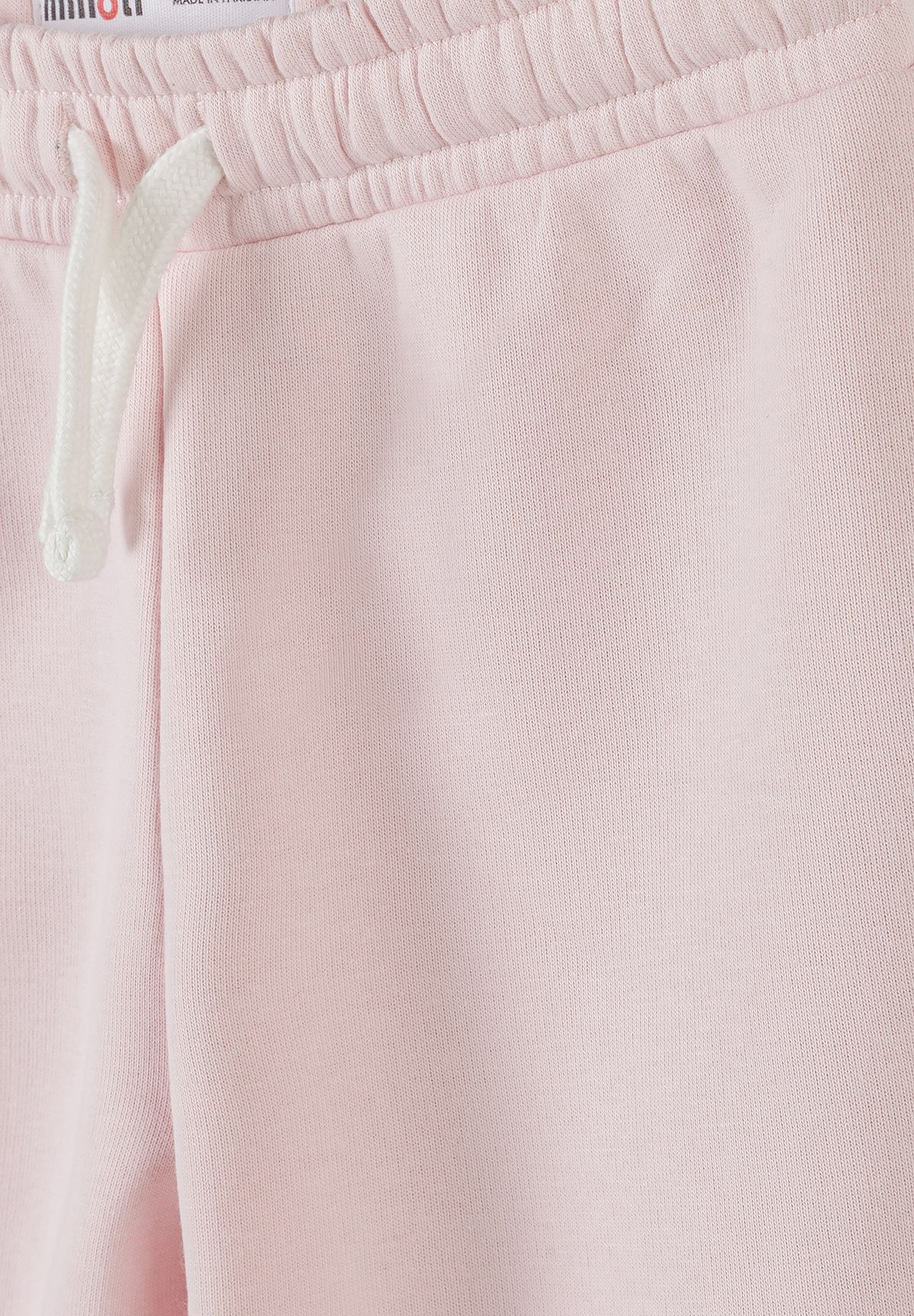 Close-up of pale pink joggers' gathered waistband, white drawstring and side pocket opening.