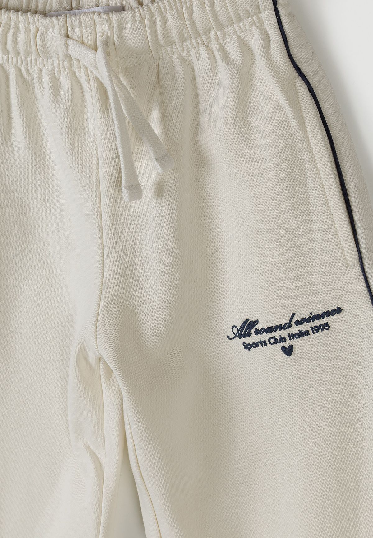 Detail of cream jogging bottoms with elastic waistband and logo embroidery.