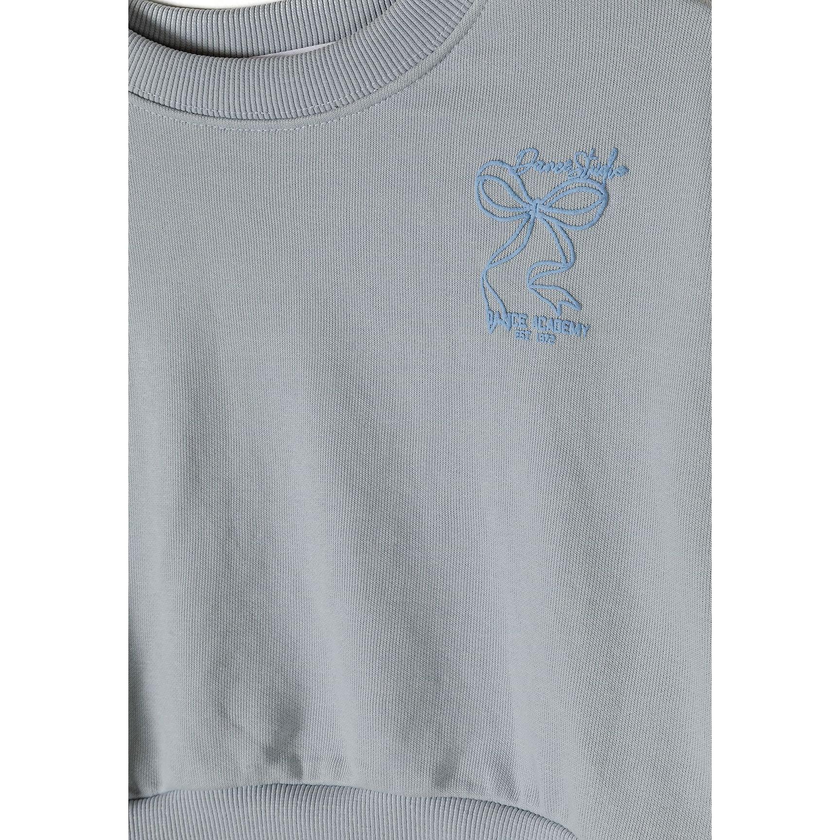 Close-up detail of light blue fabric showing small embroidered California palm tree graphic near neckline