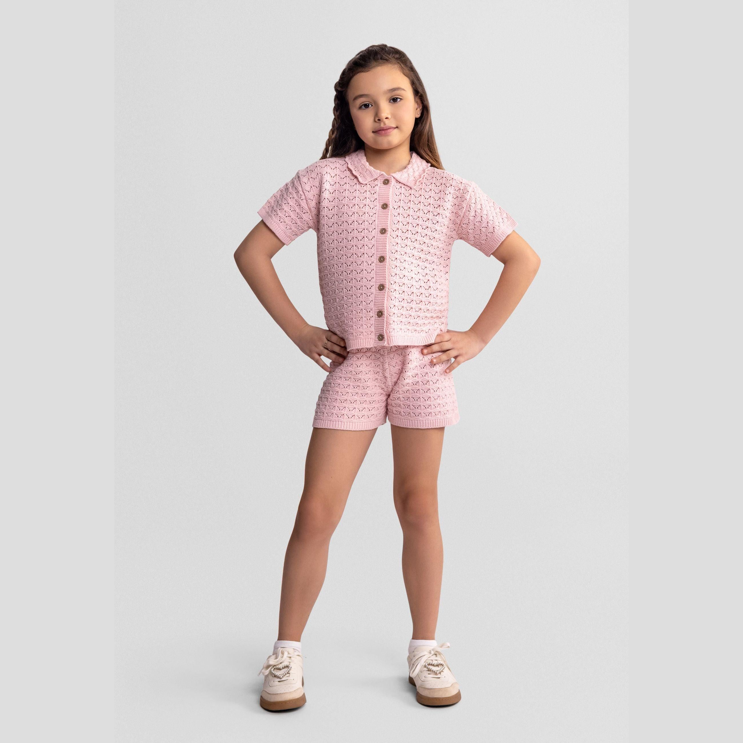 Young girl wearing blush pink pointelle knit set with button front cardigan and matching shorts, standing confidently against white background