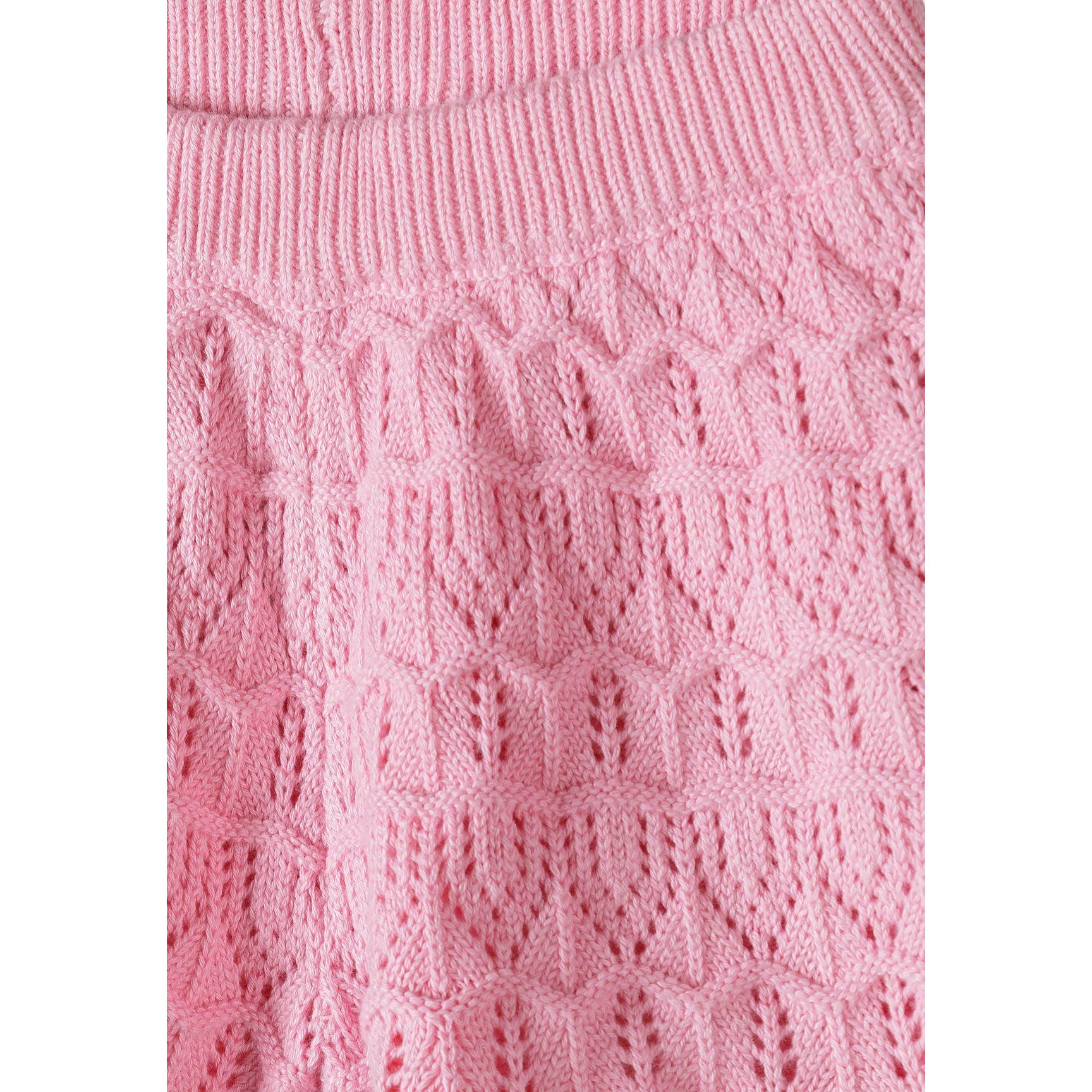 Close-up detail of pink crochet fabric showing intricate openwork stitch pattern with ribbed trim at top edge