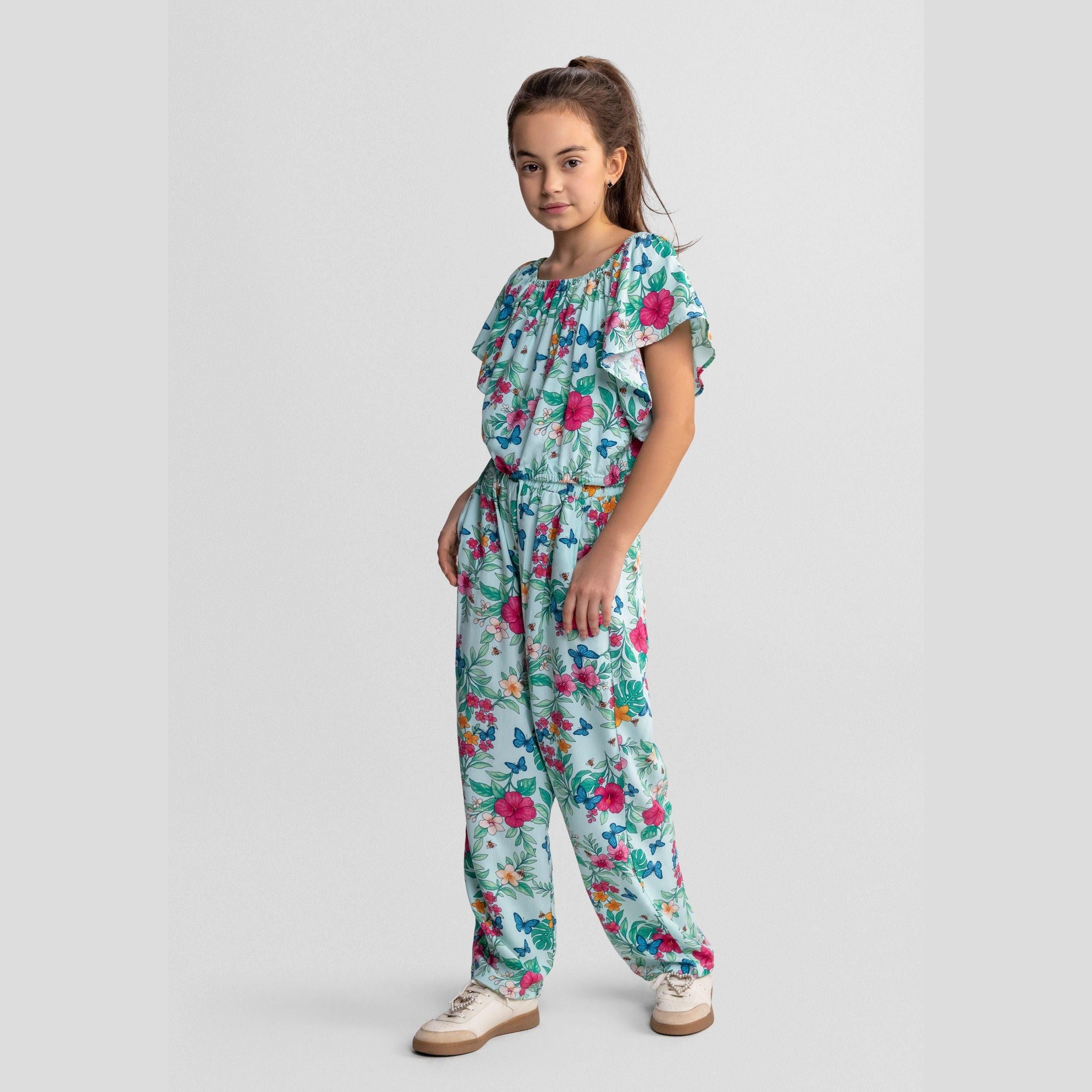 Young girl wearing mint tropical print viscose set with flutter sleeves and wide-leg trousers, standing against white studio background