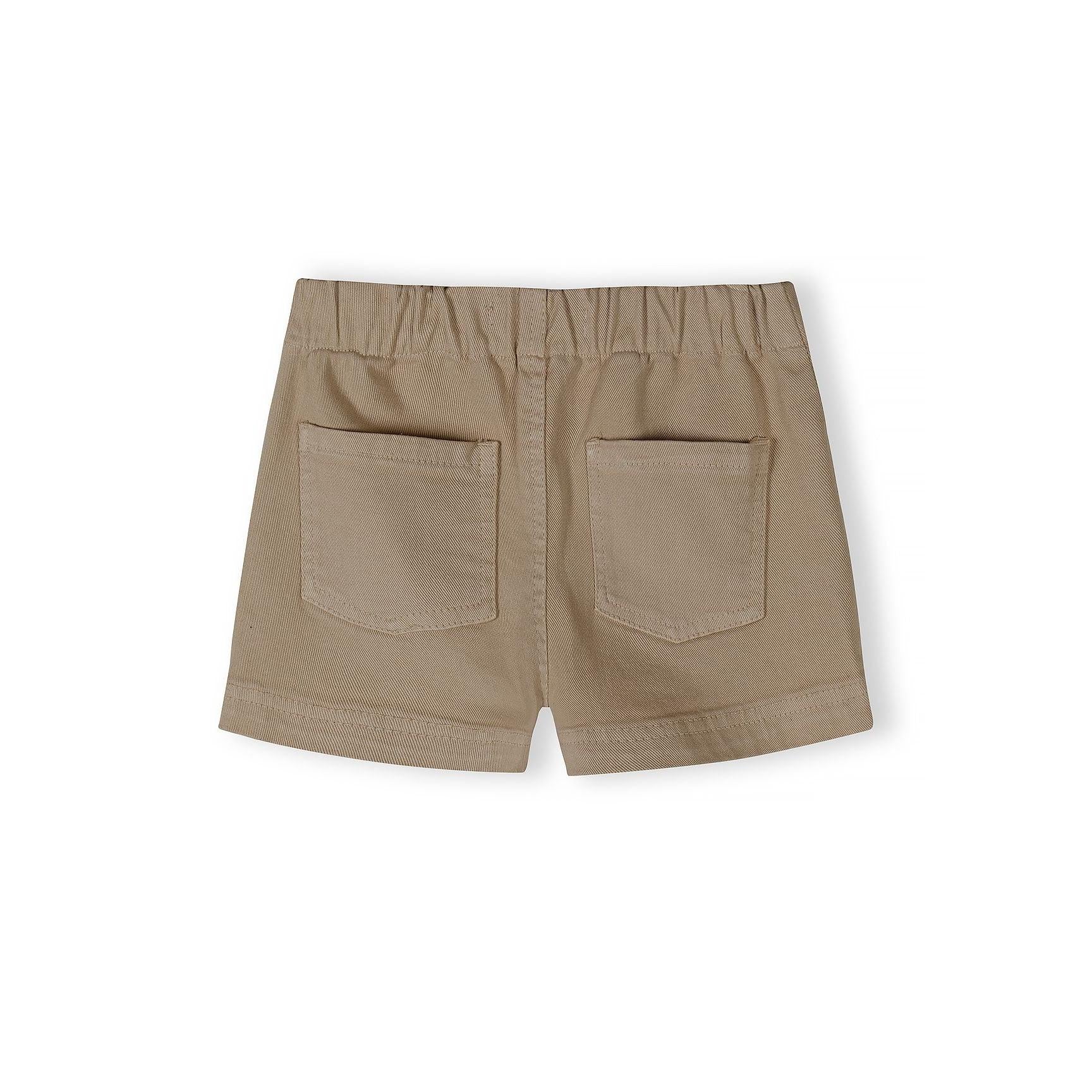 Close-up detail of white twill shorts showing button fastening, drawstring ties and fabric texture against neutral background