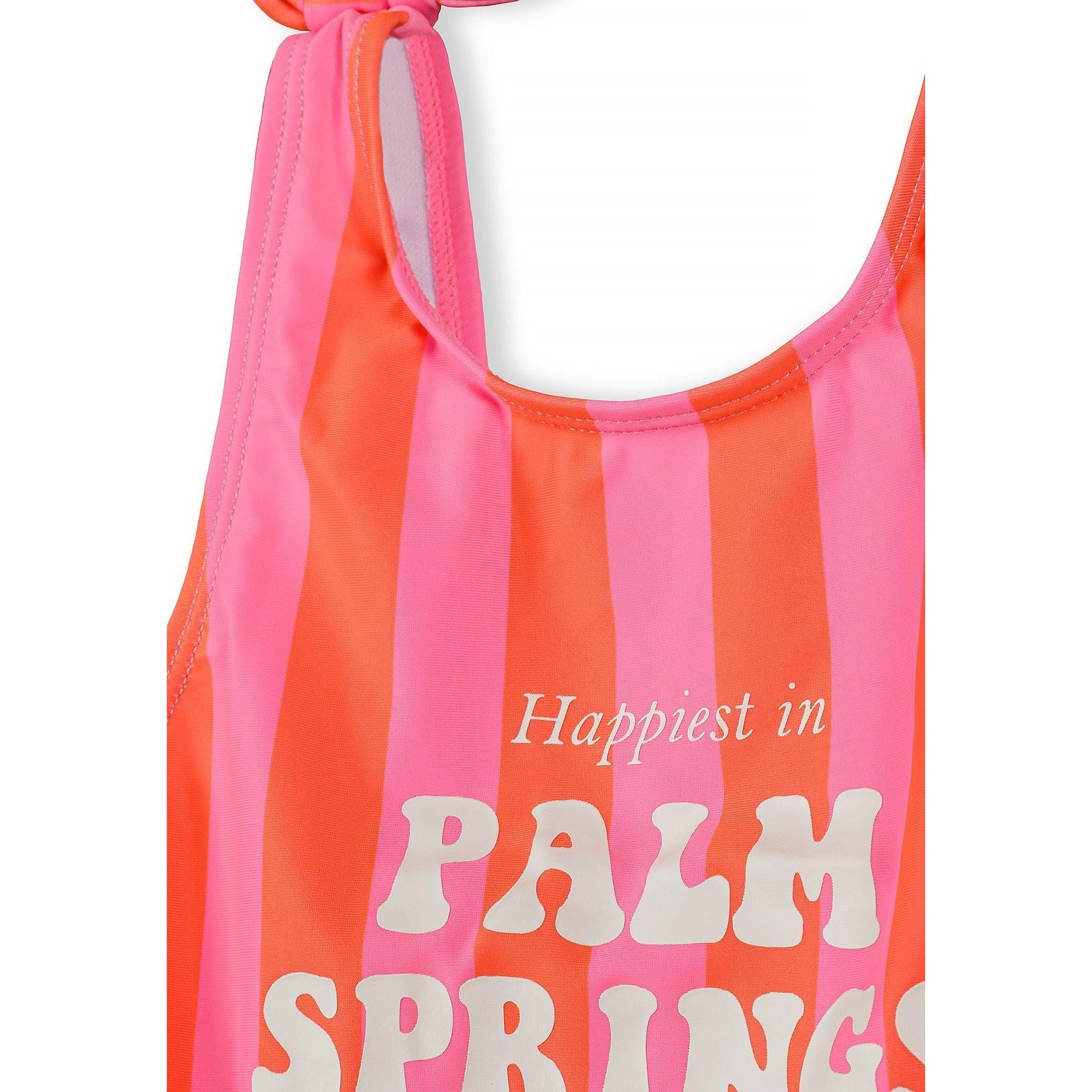 Close-up detail of pink and coral striped swimsuit showing bow-tie shoulder strap and partial 'Palm Springs' text against white background