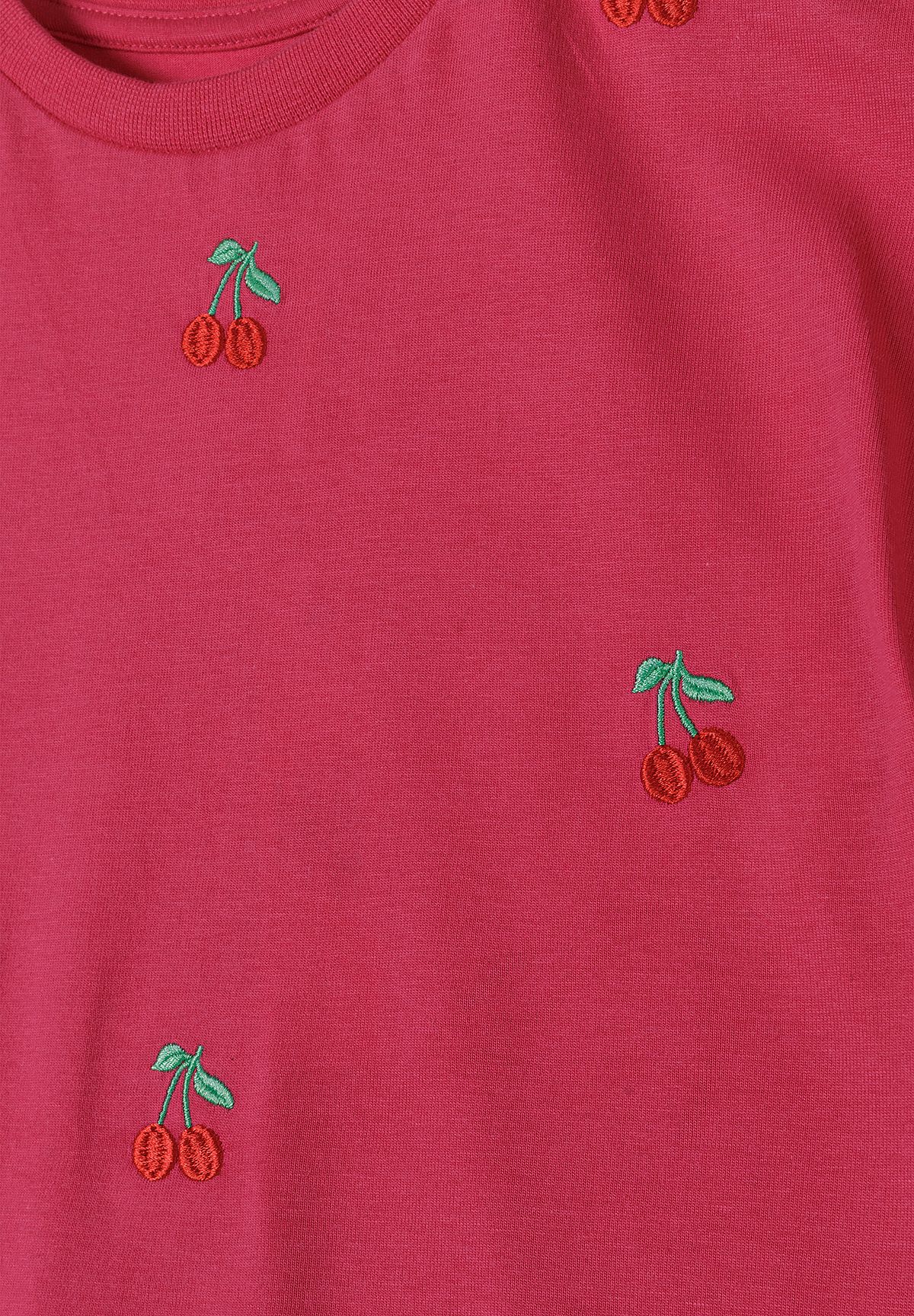 Close-up of small red cherry embroidery with green leaves on dark-pink jersey T-shirt.