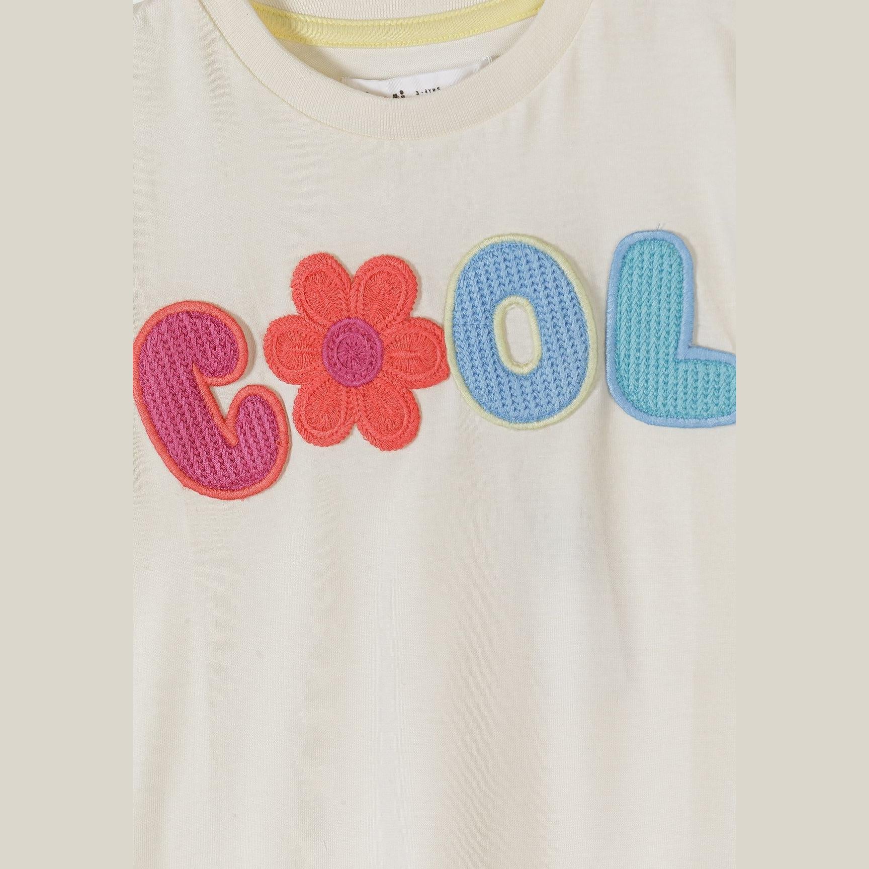 Close-up detail of colourful crochet appliqué showing 'COOL' lettering with pink, coral and blue stitching plus flower motif