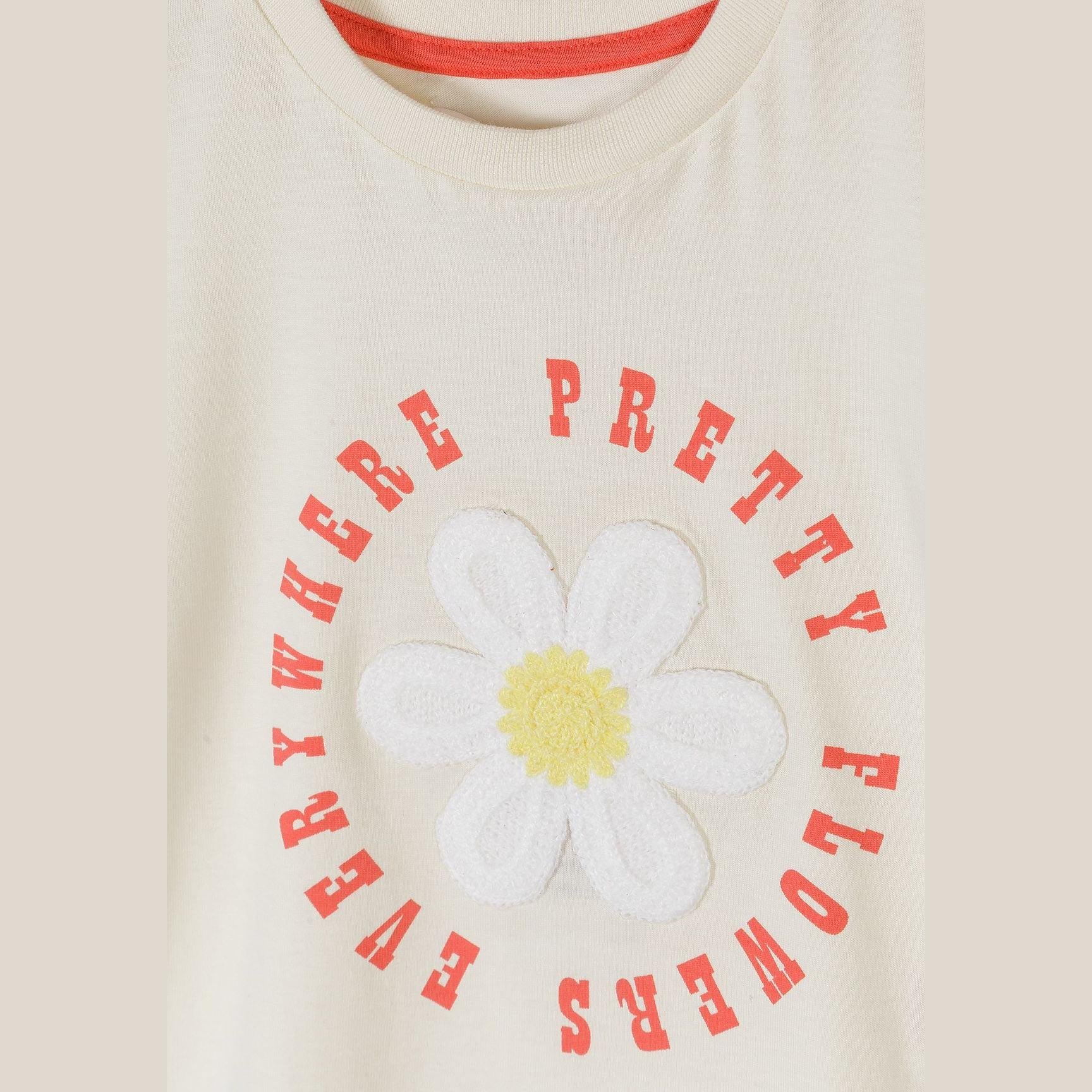 Close-up detail of white crochet daisy flower applique with yellow centre and red 'PRETTY FLOWERS EVERYWHERE' text arranged in circle