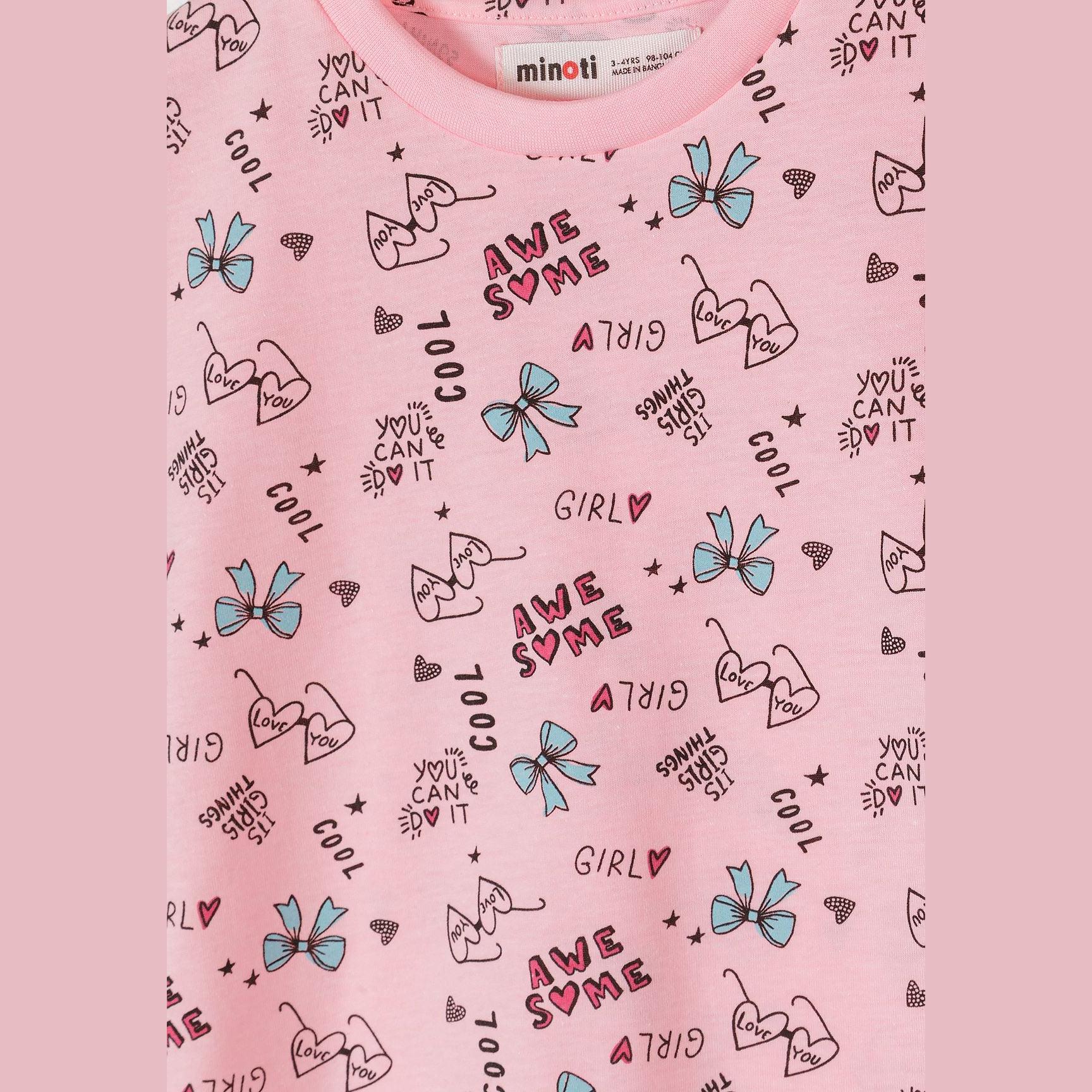 Close-up detail of pink cotton t-shirt fabric showing bow print pattern with blue bows, text elements including 'AWESOME', 'GIRLY', 'COOL' and heart shapes scattered across pink background
