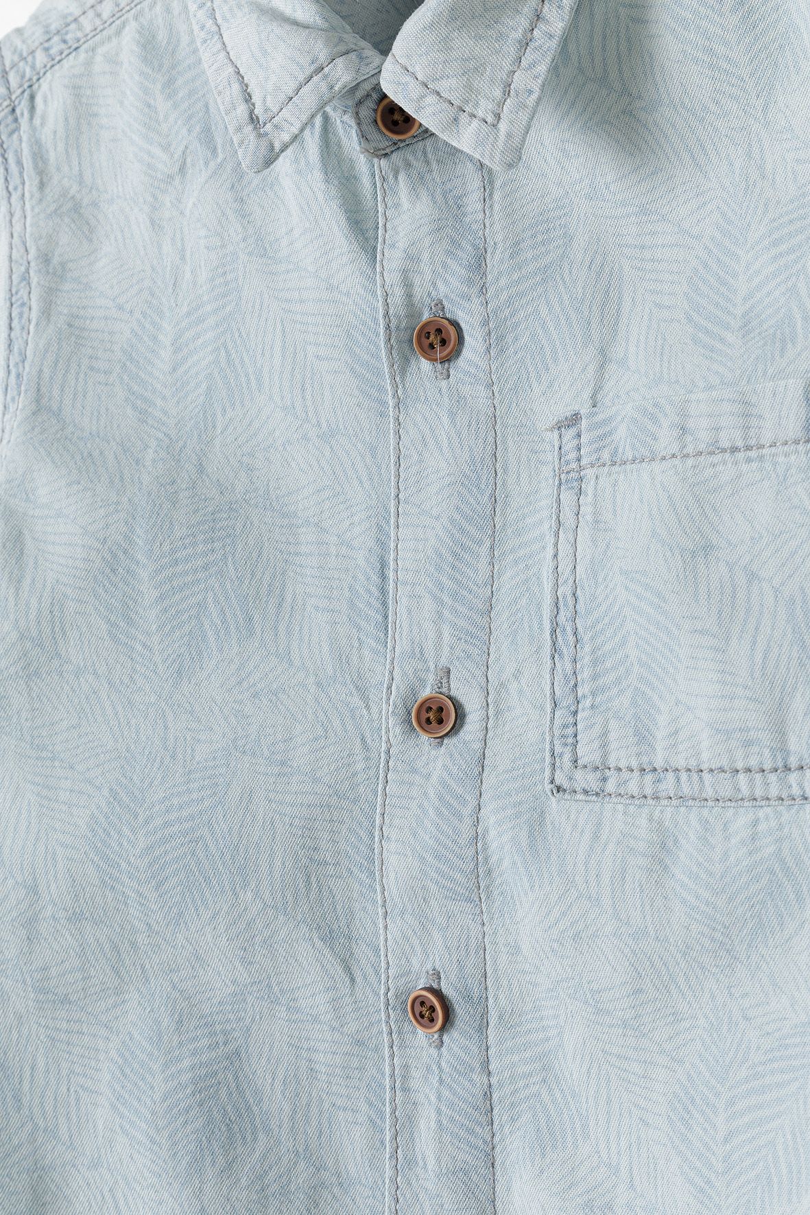 Close-up of light blue shirt's tonal leaves, brown buttons and patch pocket.