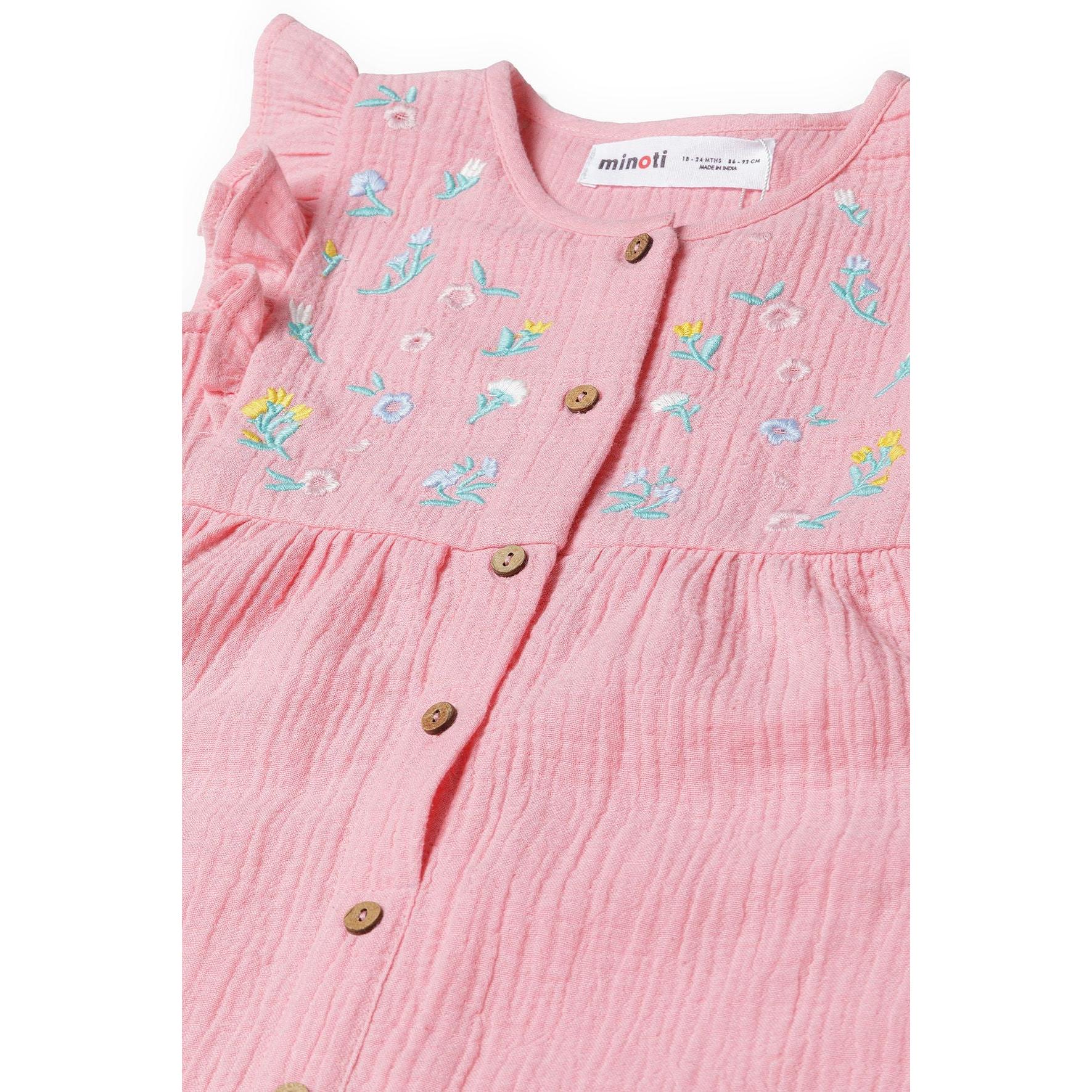 Close-up detail of pink jumpsuit showing Minoti label, blue and yellow floral embroidery pattern, and wooden button details