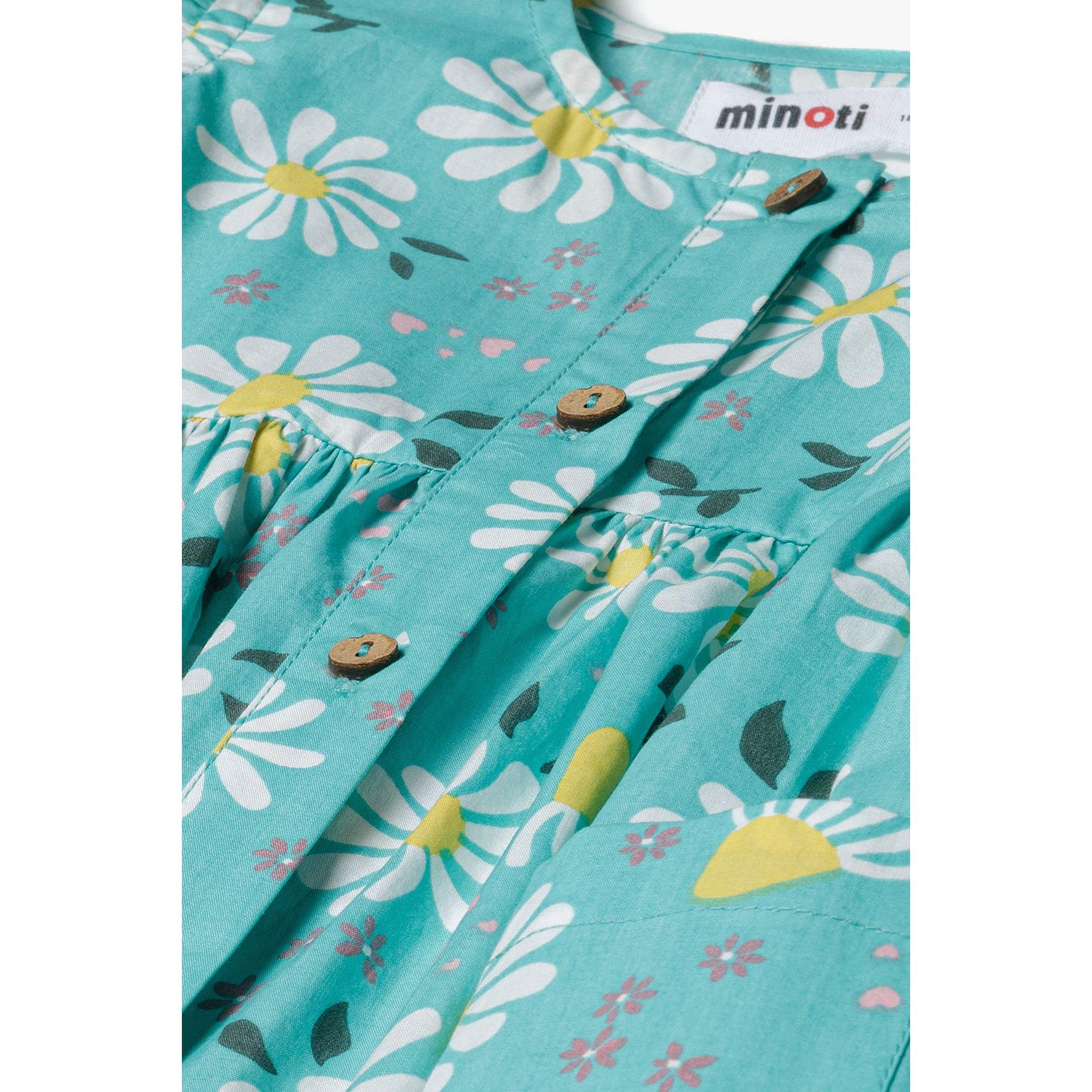 Close-up detail of turquoise fabric with white daisy print showing Minoti label and button fastening with gathered waistline
