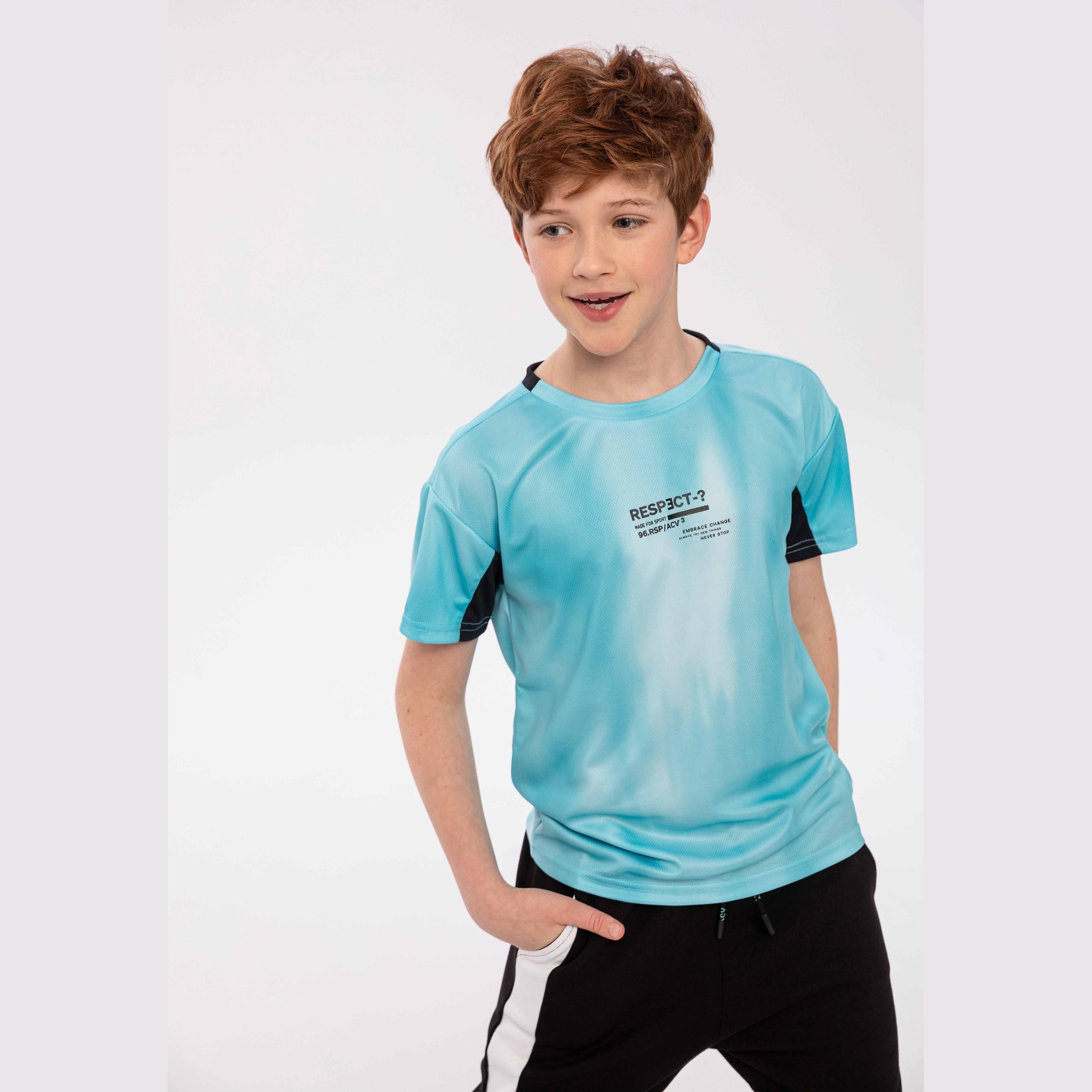 Young boy wearing mint green sports mesh t-shirt with navy contrast panels, paired with black track pants with white stripe, posed against white studio background