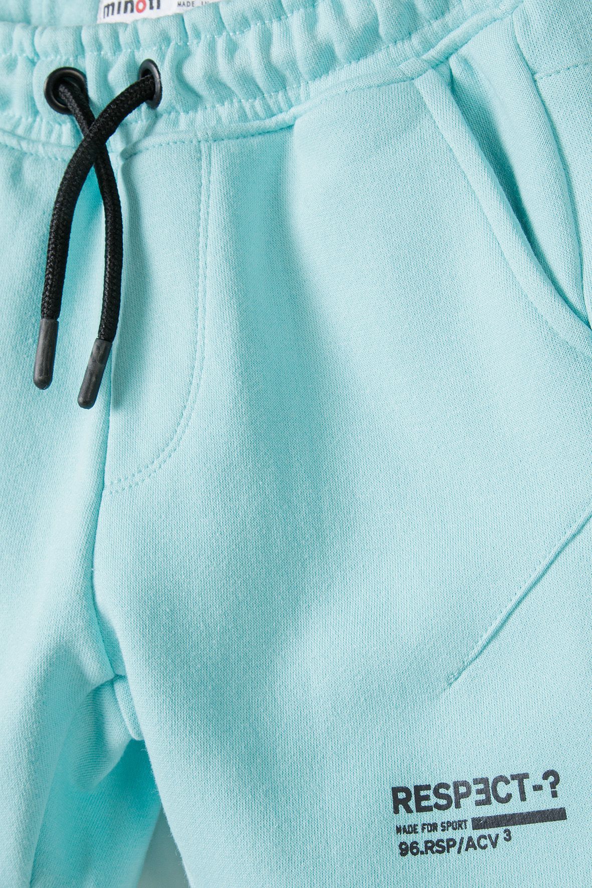 Close-up of mint shorts' black drawcord, angled pocket and text print.