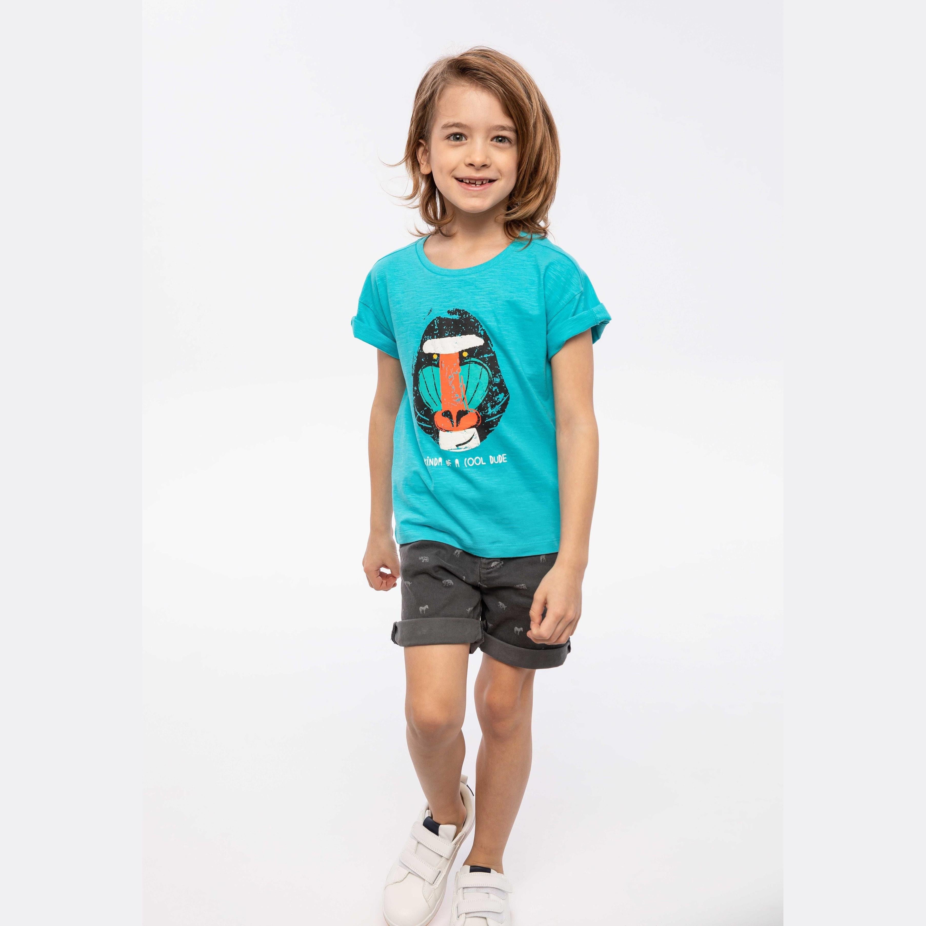 Young girl wearing turquoise oversized slub t-shirt with sloth print and grey star-patterned shorts, standing against white studio background