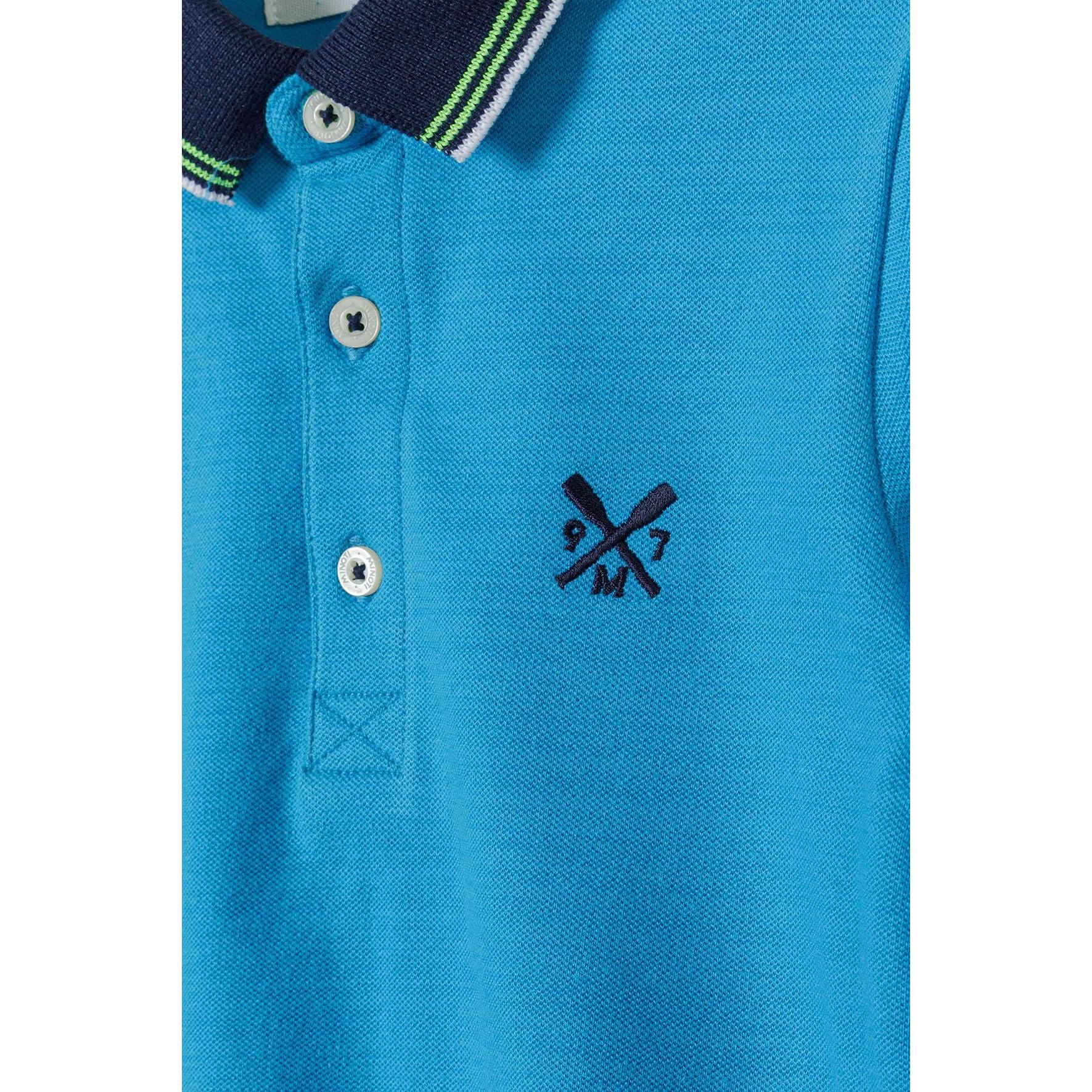 Close-up detail of turquoise polo shirt showing white button placket, navy collar with green and white stripe trim, and embroidered crossed arrows logo