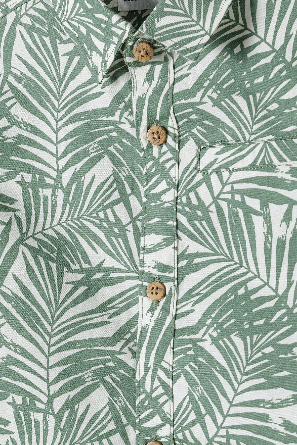 Close-up of green palm print, tan buttons and chest pocket on boys' shirt.