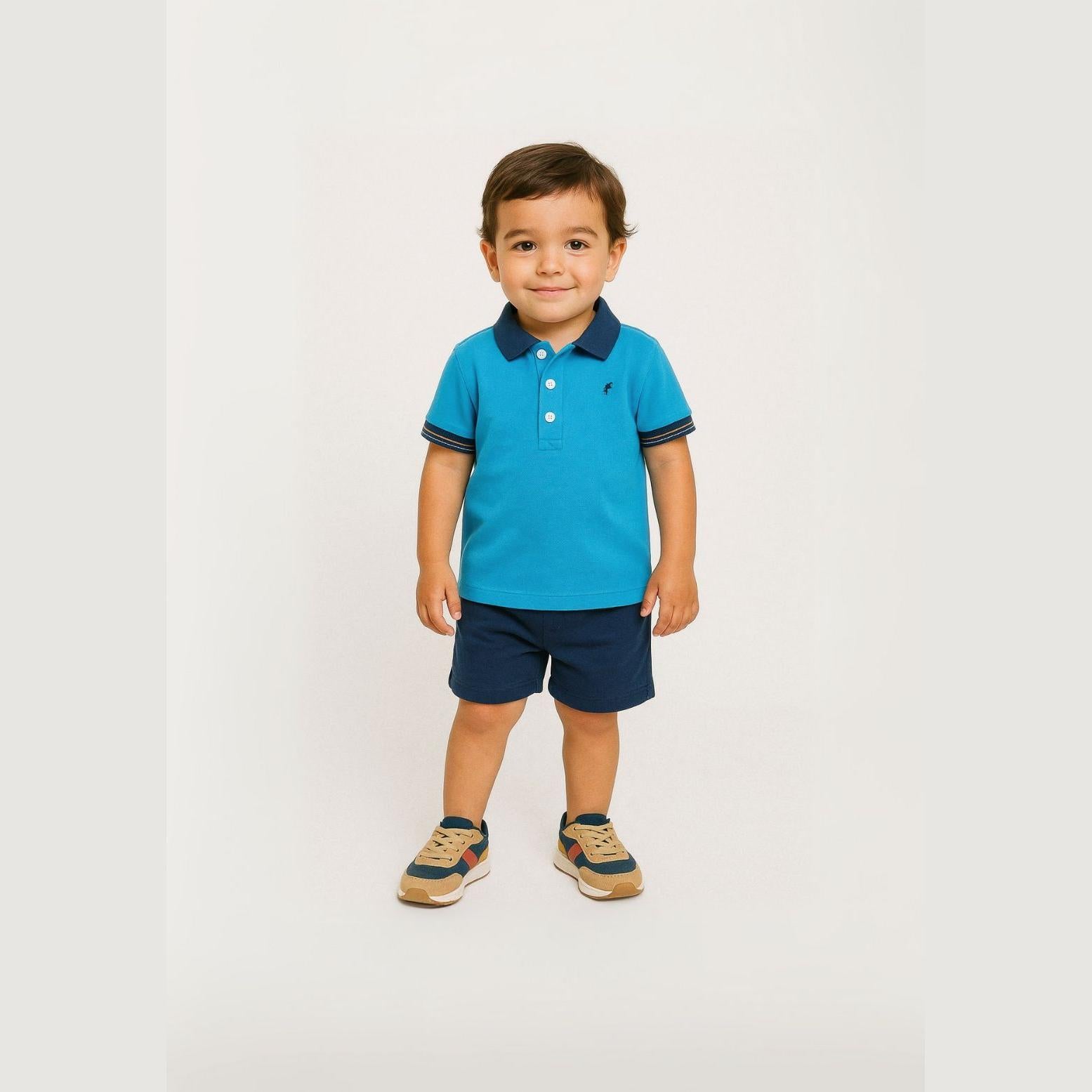 Young boy wearing turquoise polo shirt with navy collar and navy shorts, standing against white background, showing full outfit styling