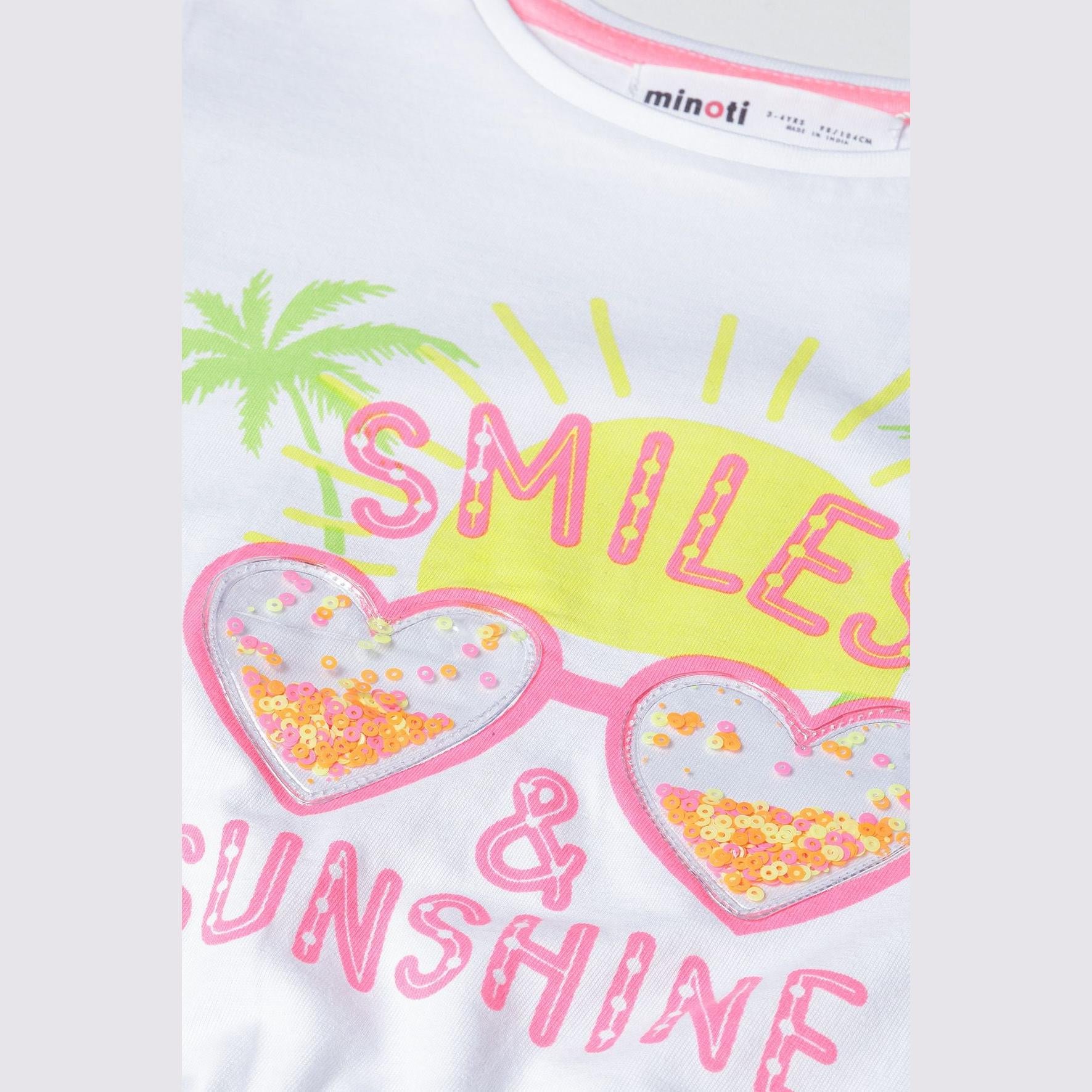 Close-up detail of white t-shirt showing neon smile and sunshine print with heart-shaped sunglasses containing sequins and Minoti label