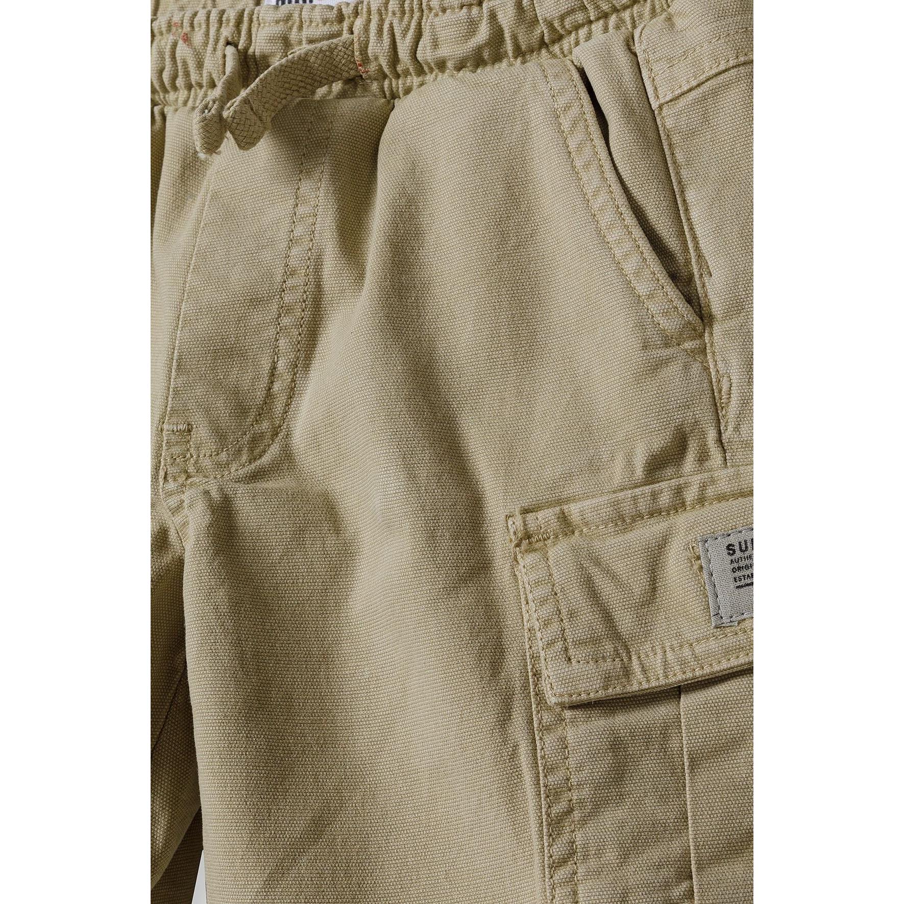 Close-up detail of khaki combat shorts showing cargo pocket with flap closure, stitching details and fabric texture