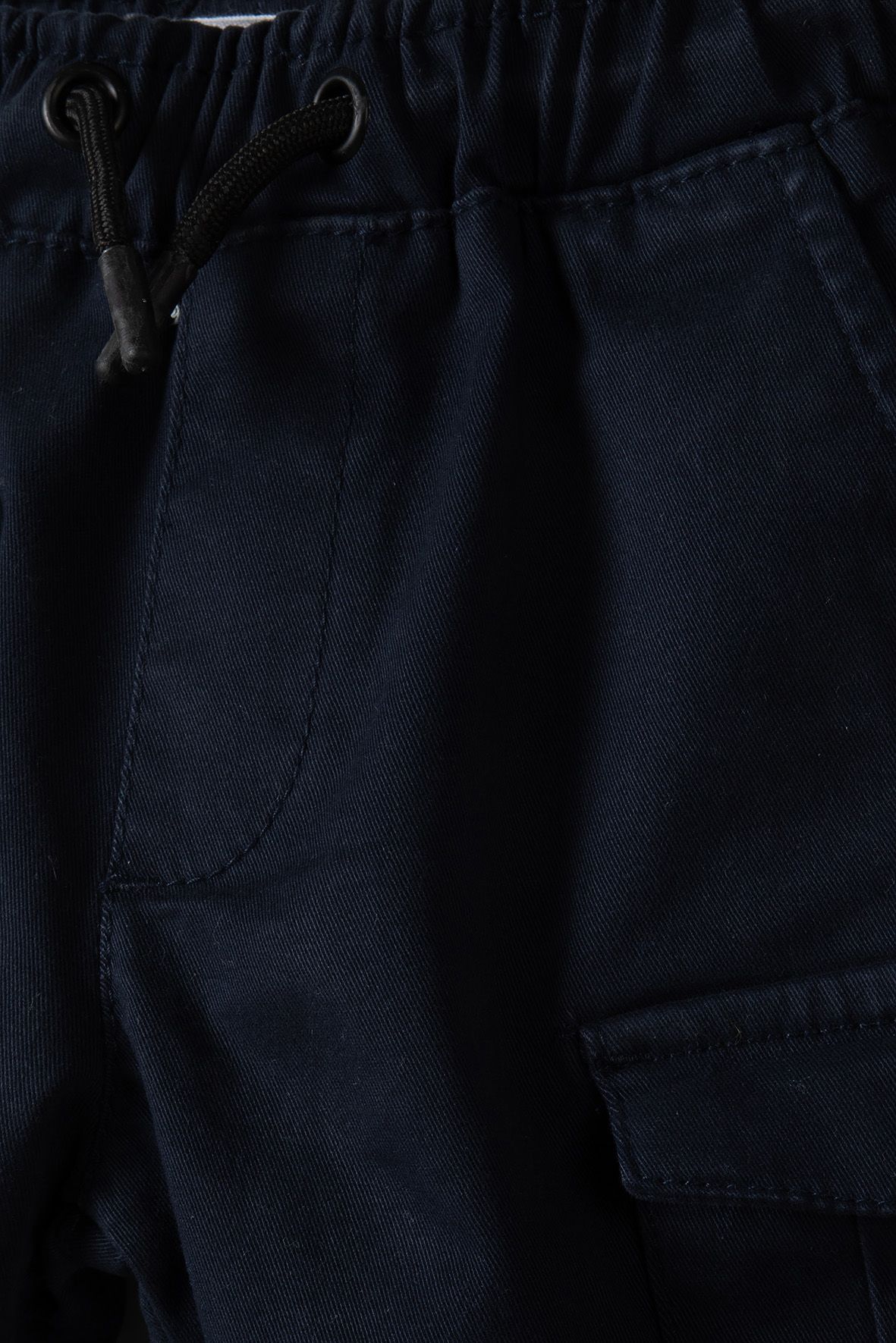 Close-up of black drawstring, gathered waistband and curved pocket on navy cargo shorts.