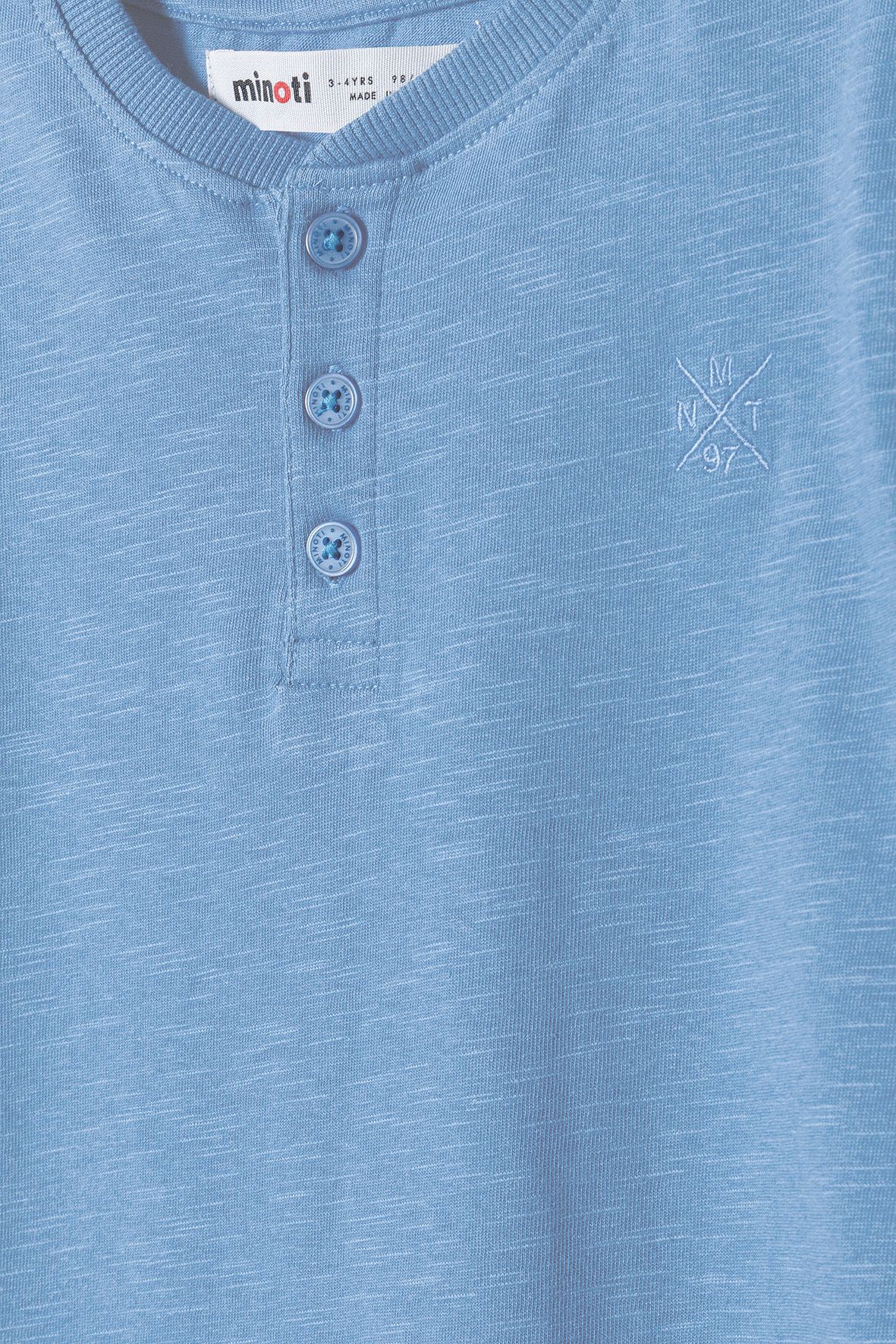 Close-up of blue henley T-shirt's three matching buttons, ribbed neck and embroidered emblem.