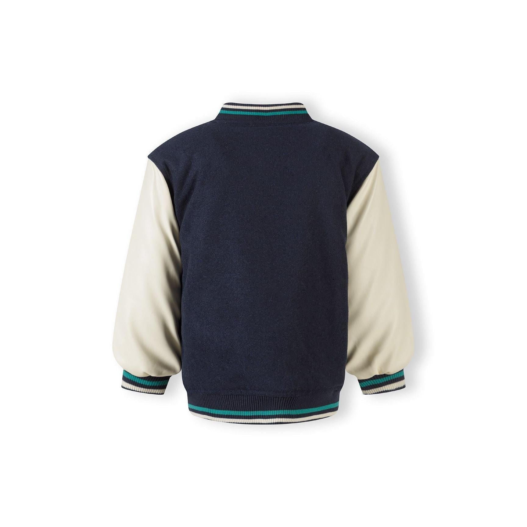 Close-up detail of green chenille M appliqué patch with NEW YORK CITY text on navy fabric background with press studs visible