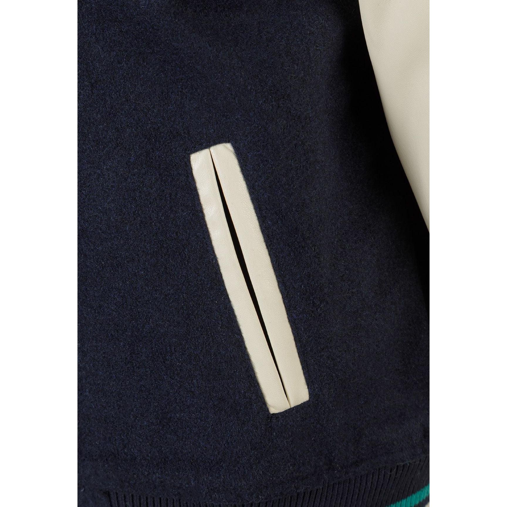 Close-up detail of green chenille M appliqué patch with NEW YORK CITY text on navy fabric background with press studs visible