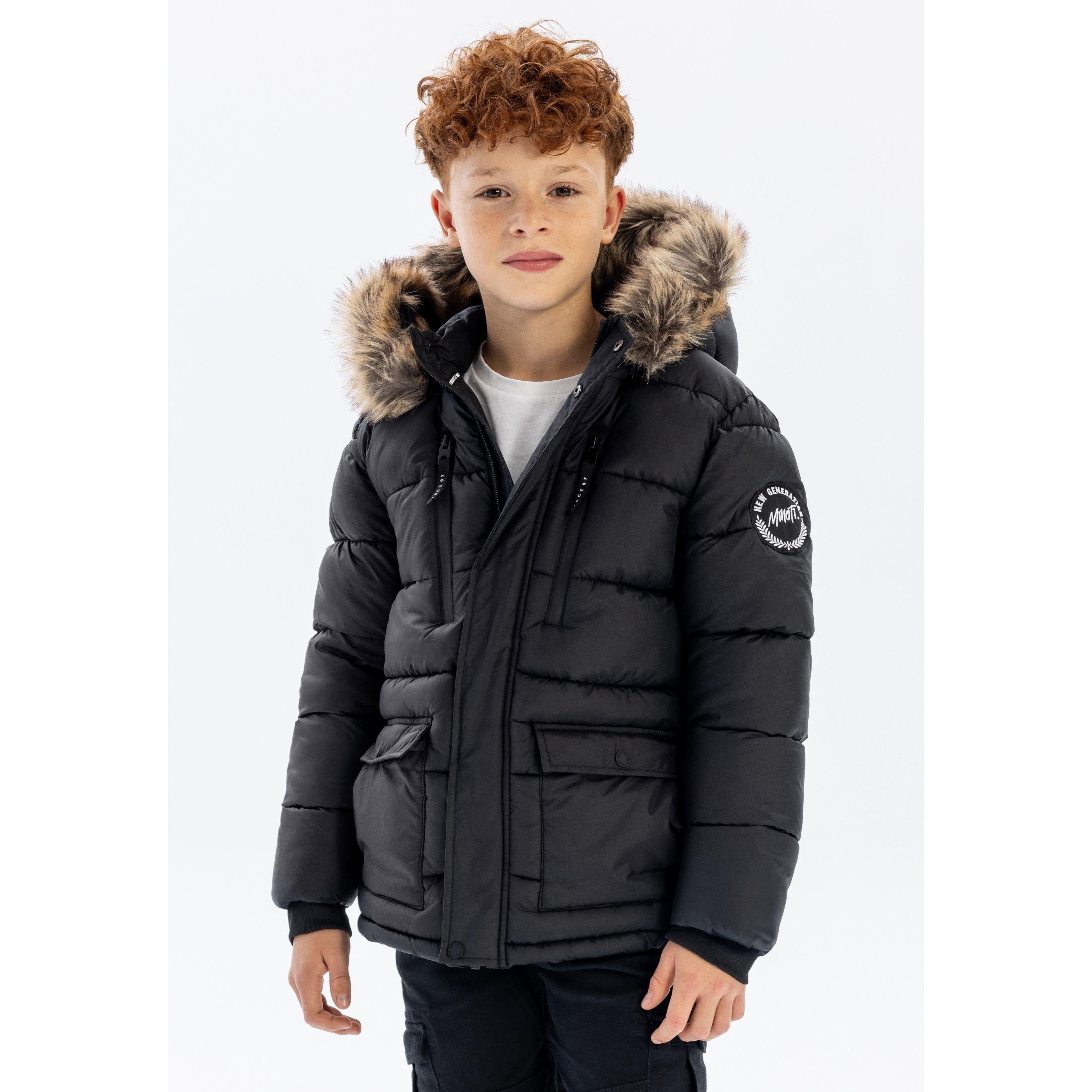 Young boy with curly hair wearing black quilted parka jacket with faux fur hood trim, standing against white background