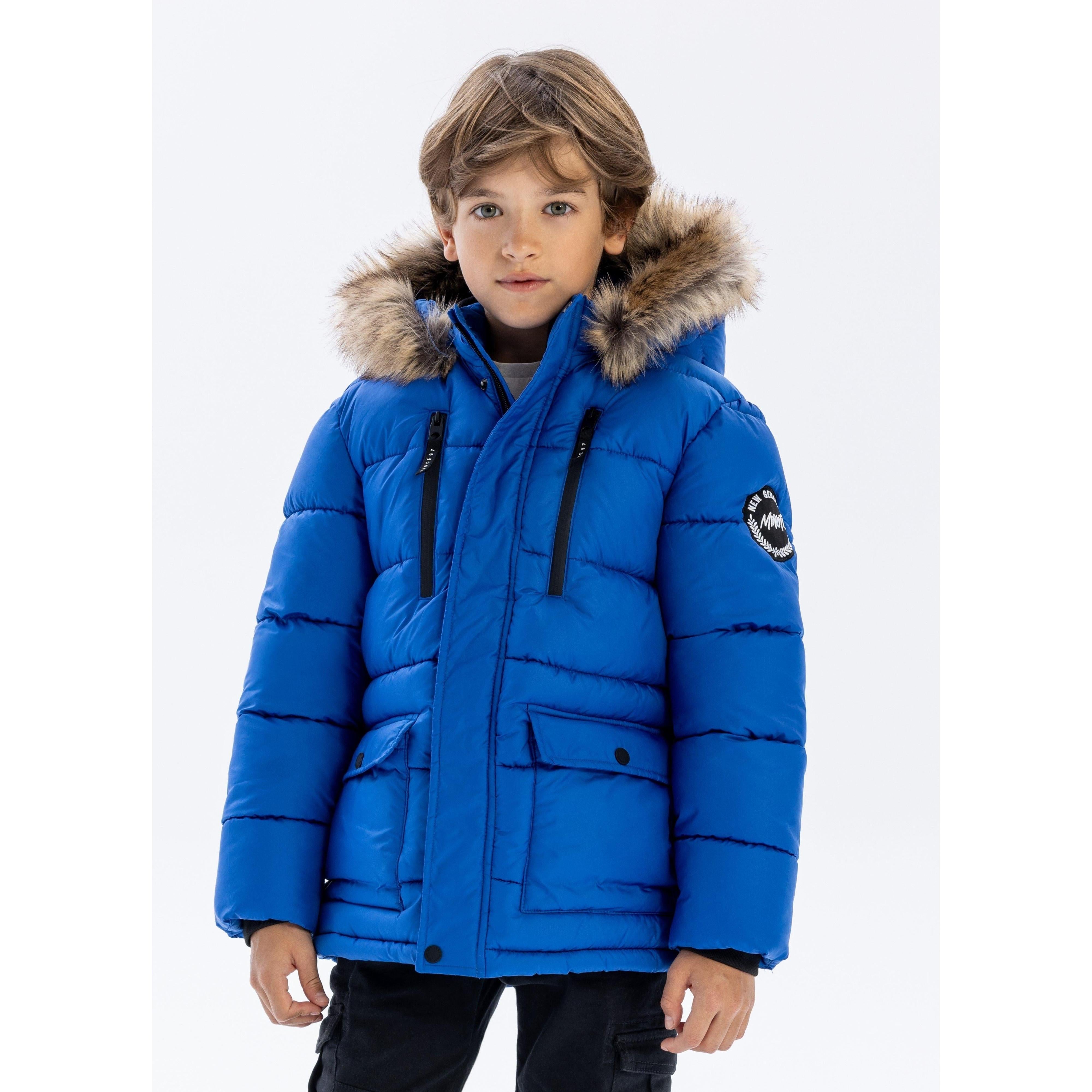 Young boy wearing cobalt blue quilted puffer jacket with faux fur hood trim, standing against white background